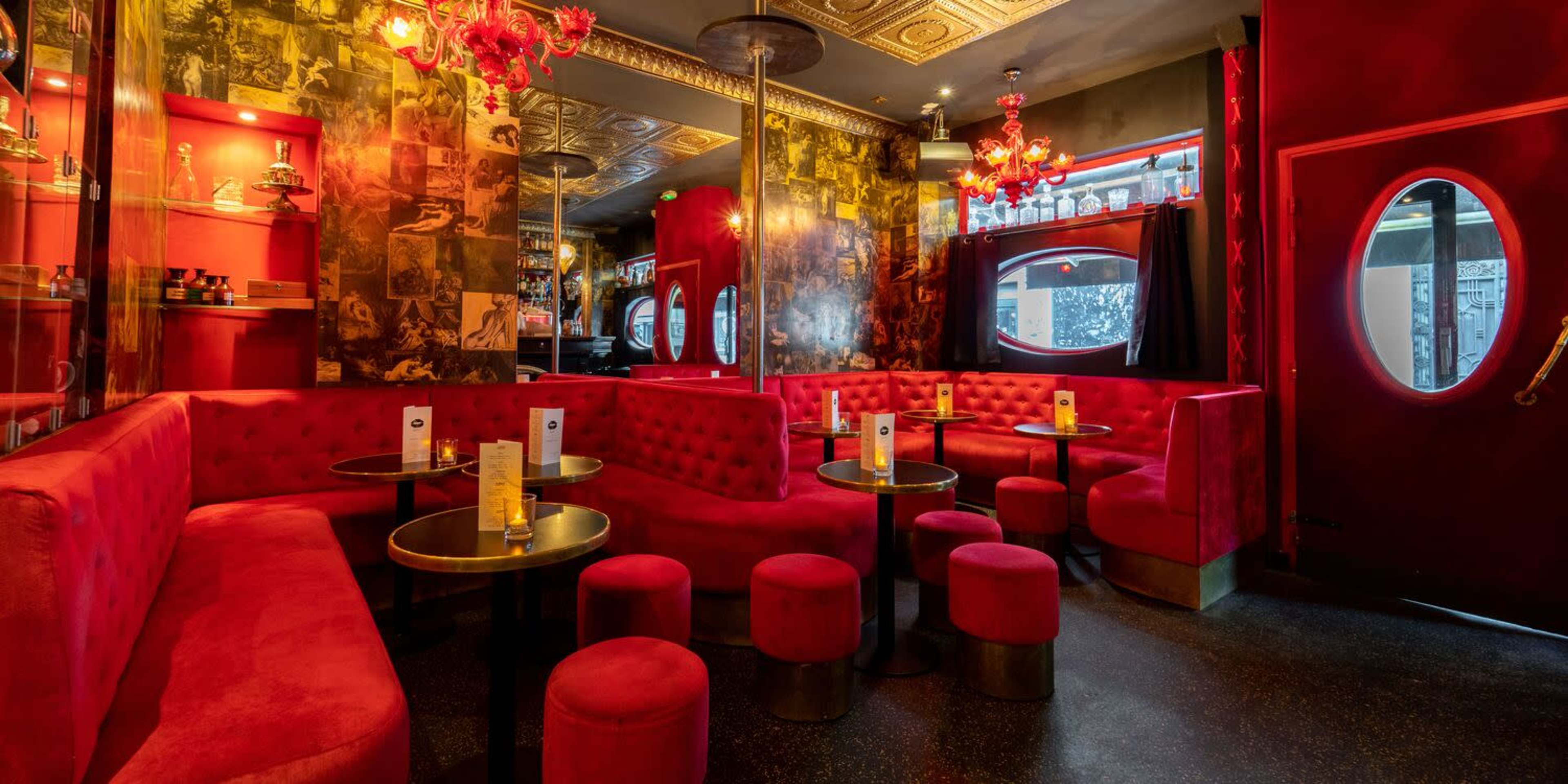 A vibrant lounge features red seating and decor, with round tables and dim lighting.