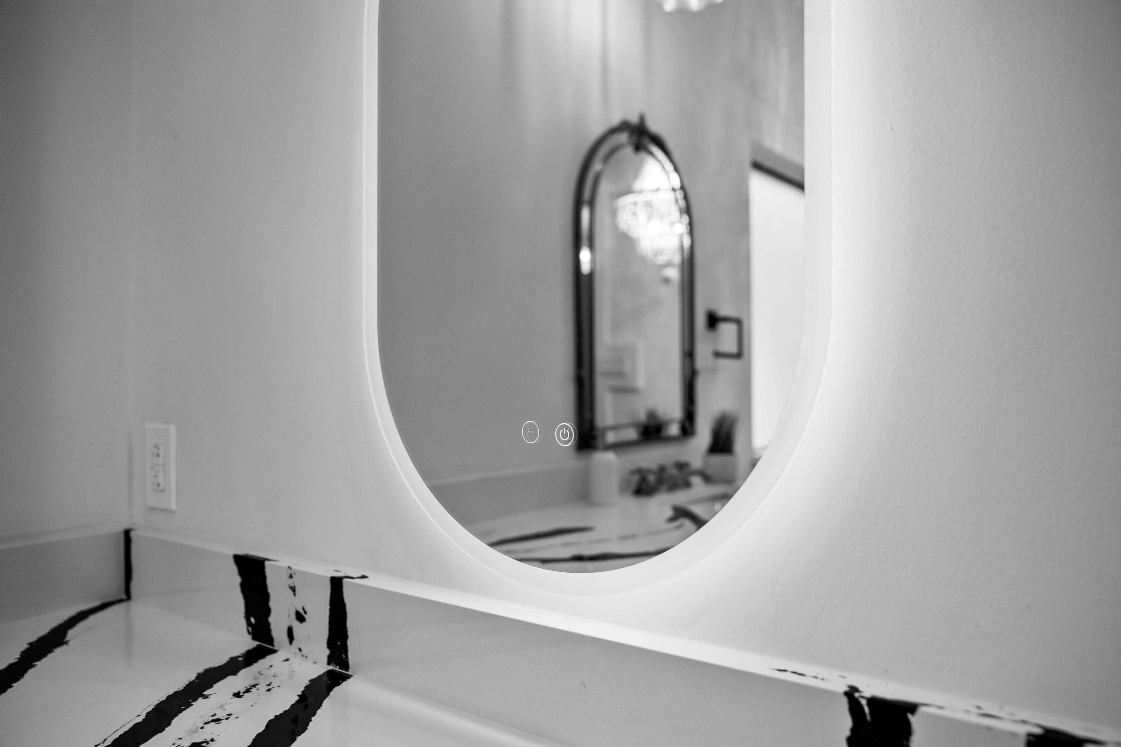 A close-up view of a bathroom countertop with a mirror reflecting a chandelier and a decorative mirror in the background.