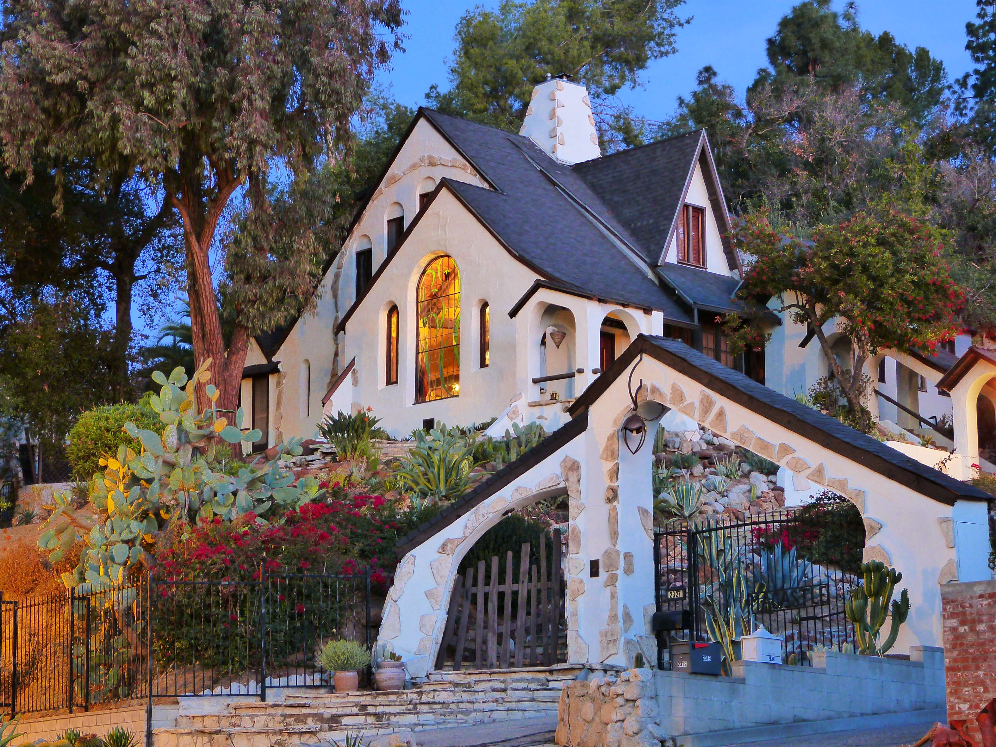 A large, decorative house with a peaked roof and stained glass windows, set on a landscaped hill.