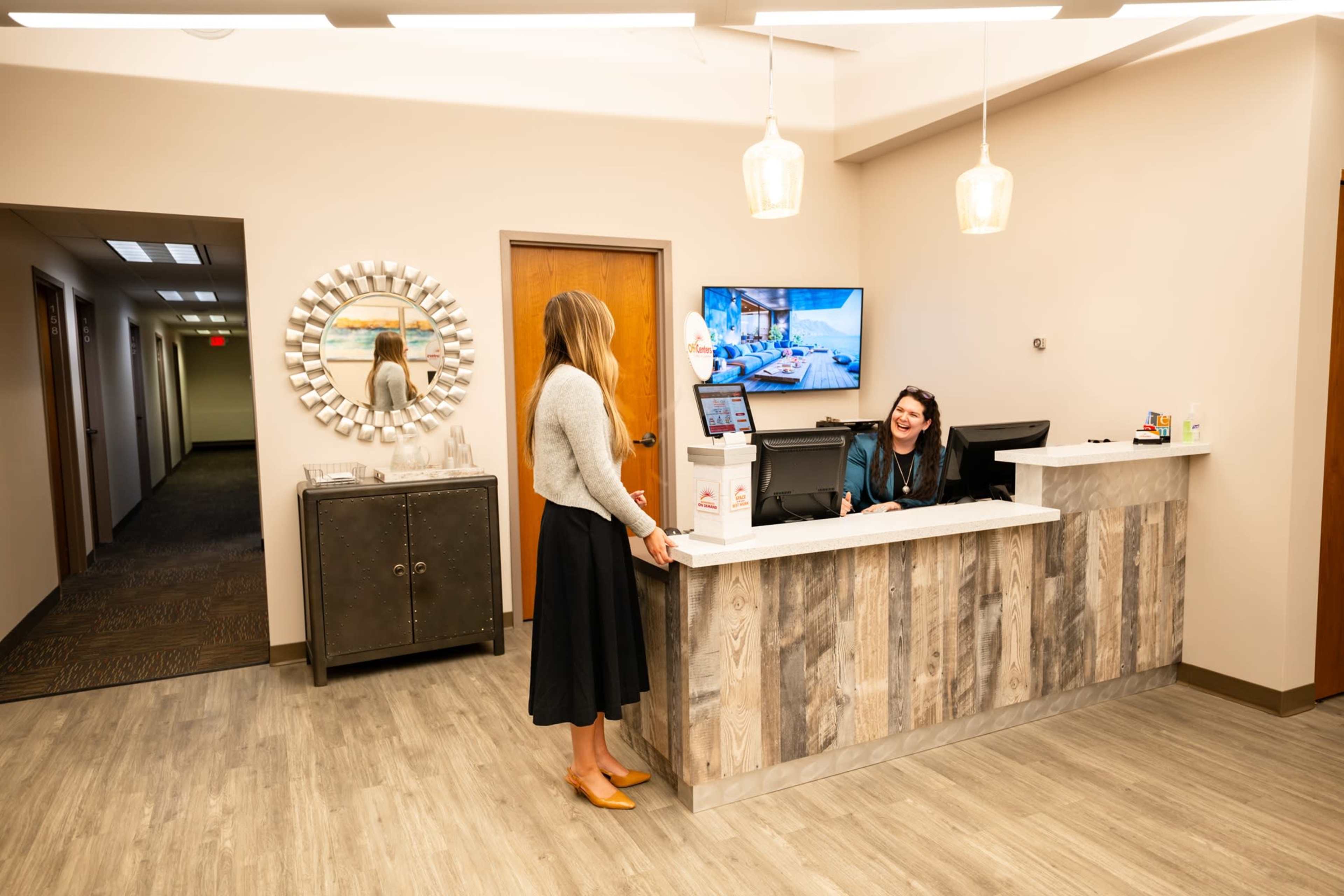 A woman in a skirt stands at a reception desk while a staff member assists her.