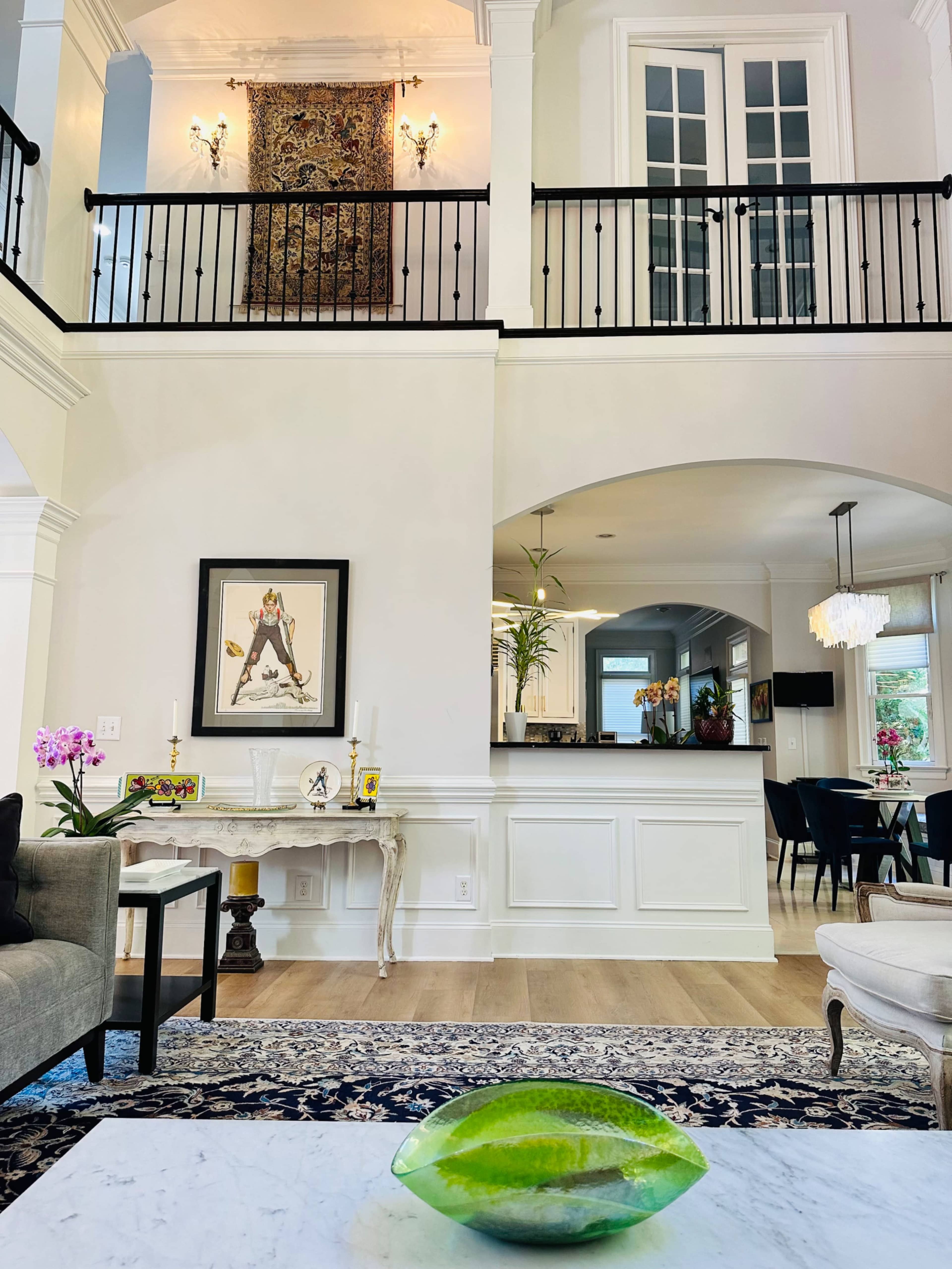 The image shows a spacious living area with a marble coffee table featuring a green decorative bowl, flanked by furniture and an open kitchen in the background.