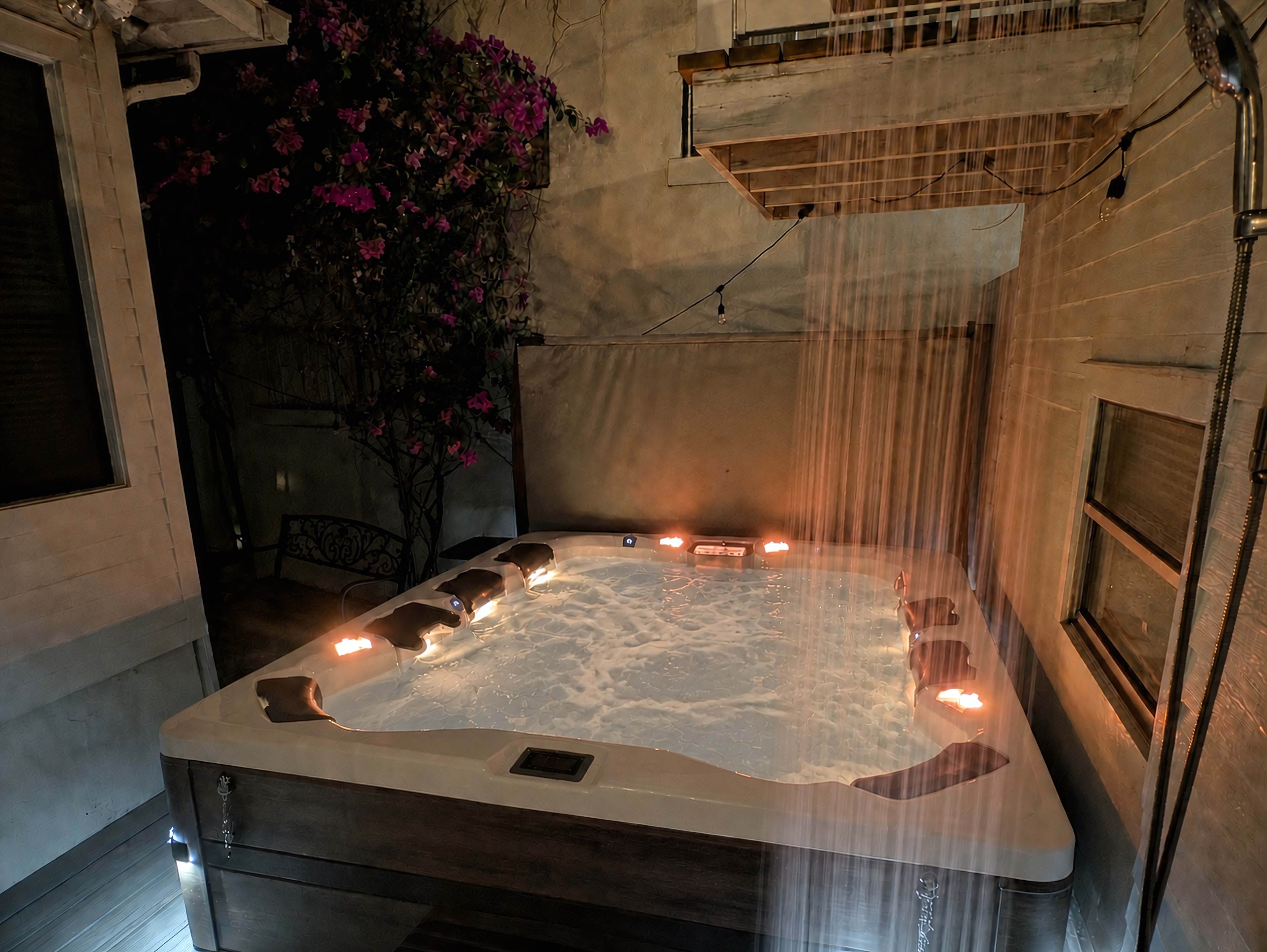 A hot tub surrounded by a wall adorned with blooming bougainvillea sits beneath a covered area with a waterfall feature.