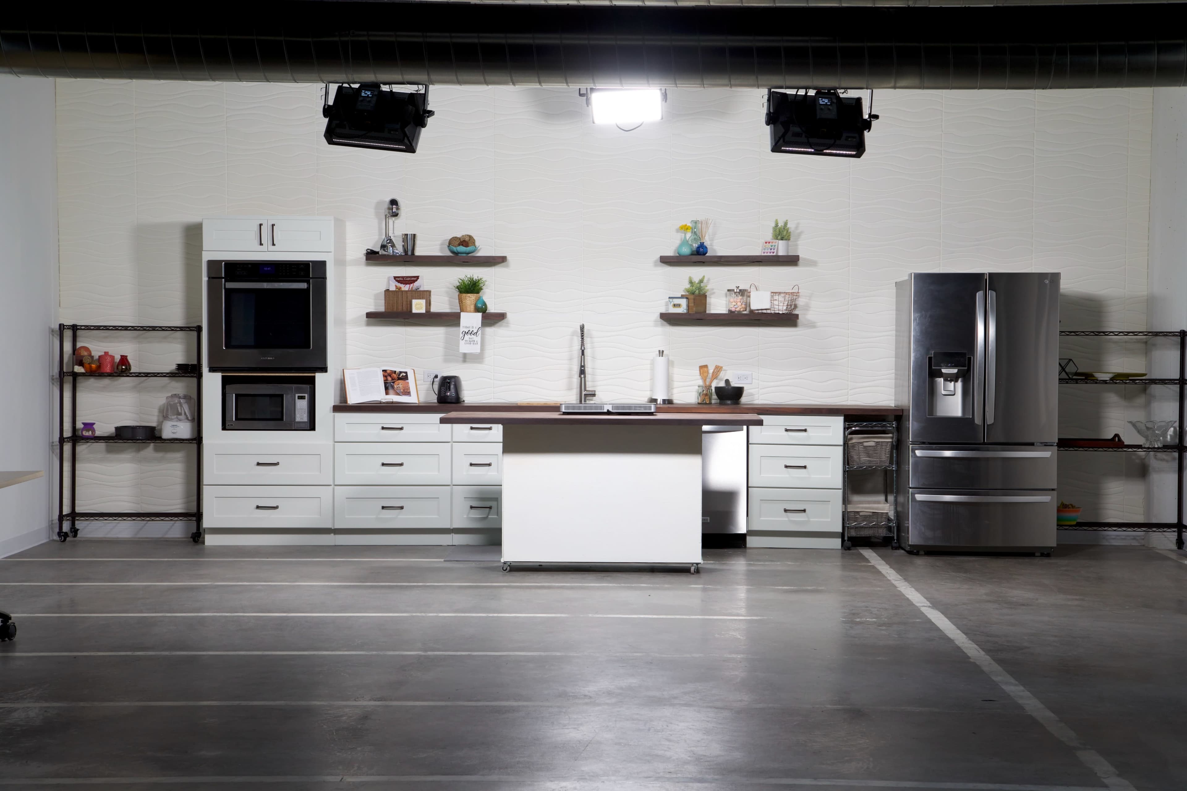 A modern kitchen setup with white cabinets, stainless steel appliances, and open shelves displaying decorative items.