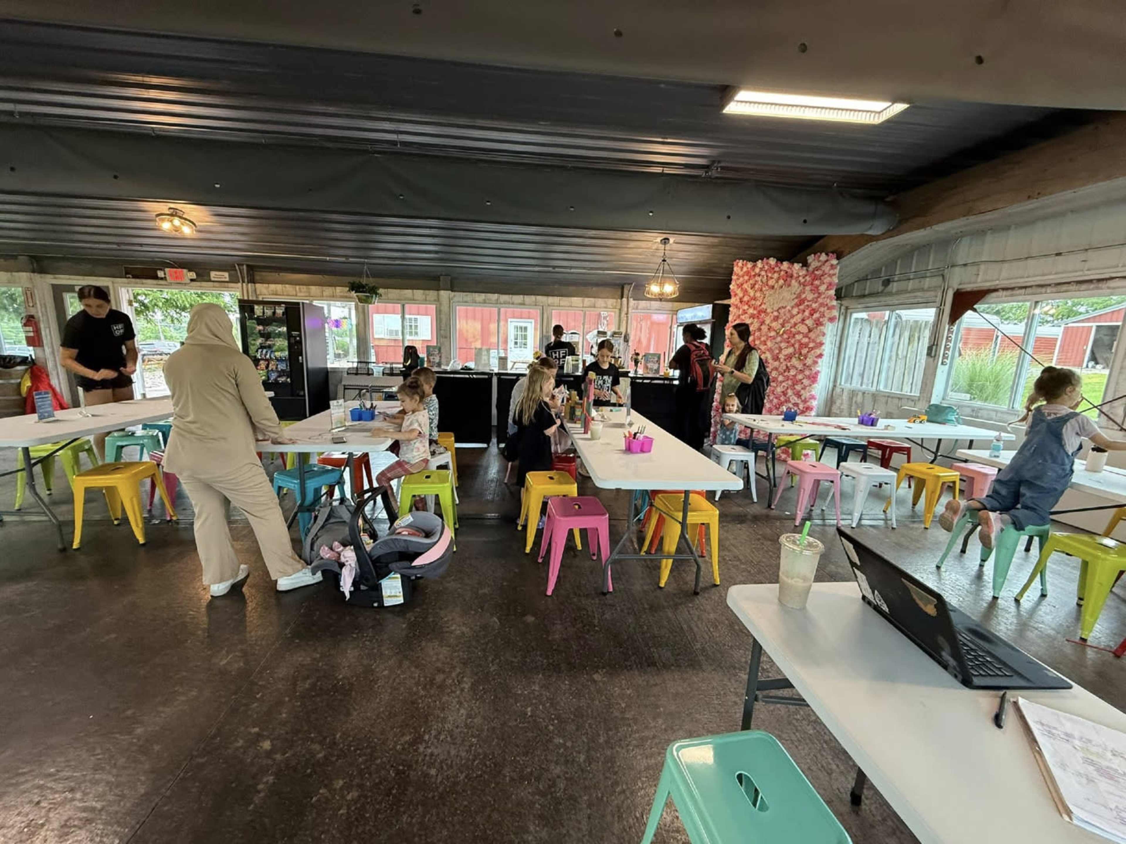 The image shows a spacious indoor area with colorful chairs and tables, where people are engaged in various activities.