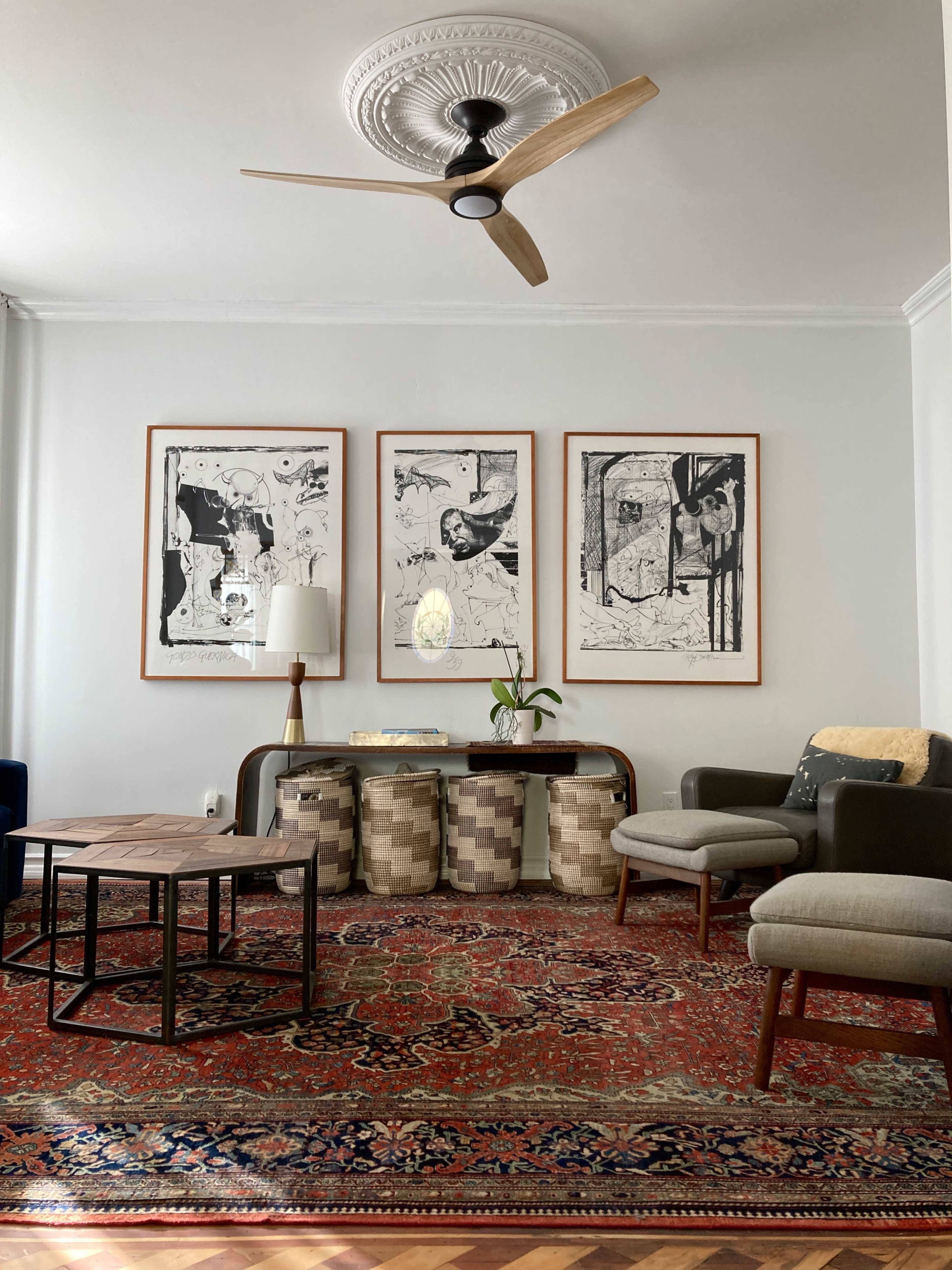 A living room with three framed artworks on the wall above a console table, flanked by a lamp and a plant, a vintage rug on the floor, and modern seating arrangements.