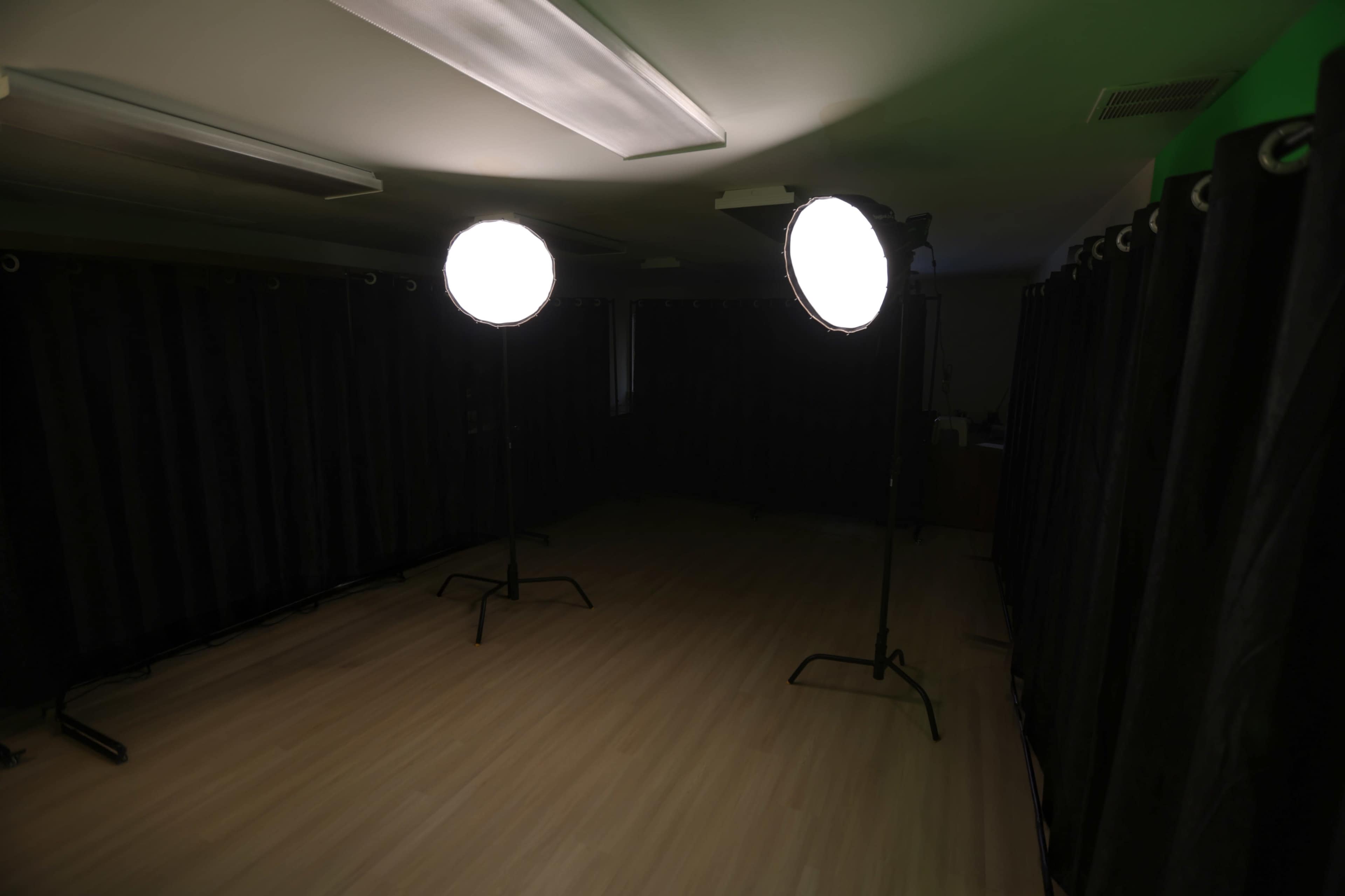 The image shows a dimly lit room with two large softbox lights set up on stands, surrounded by black curtains.