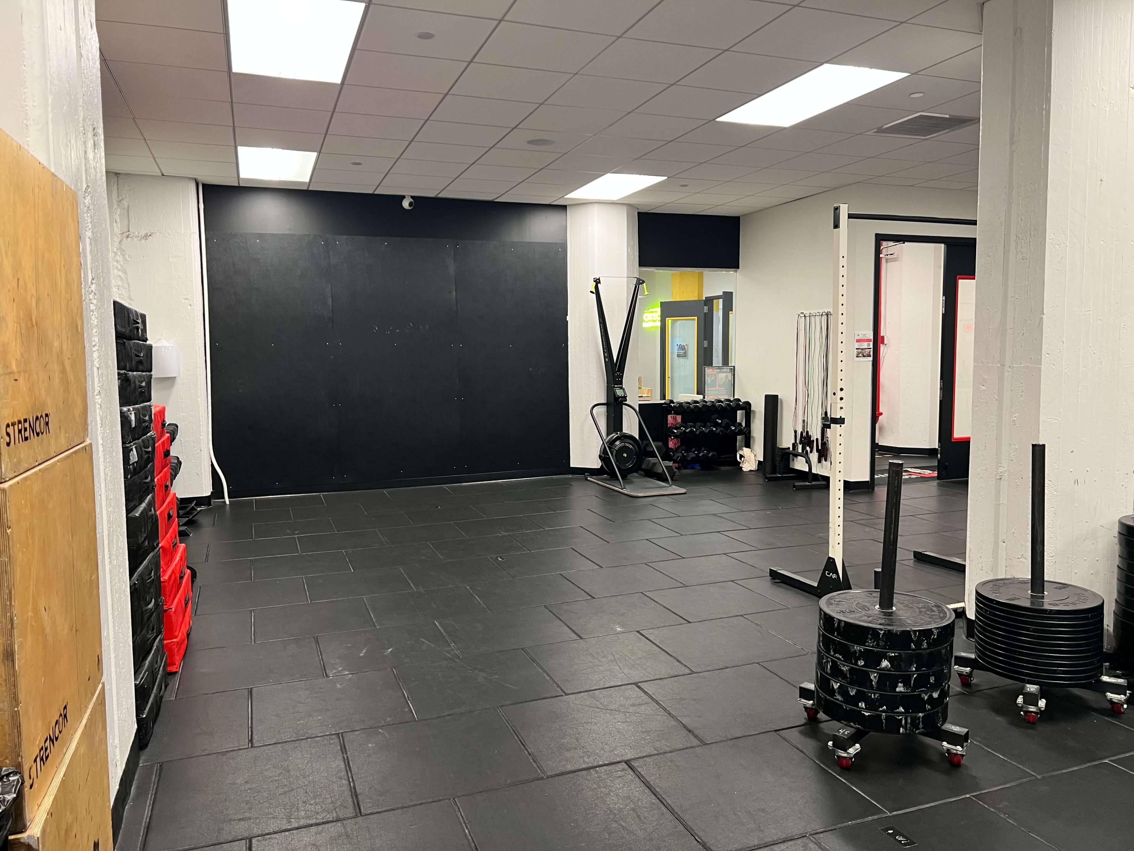 A spacious gym interior with black flooring, weightlifting equipment, and a functional training area.