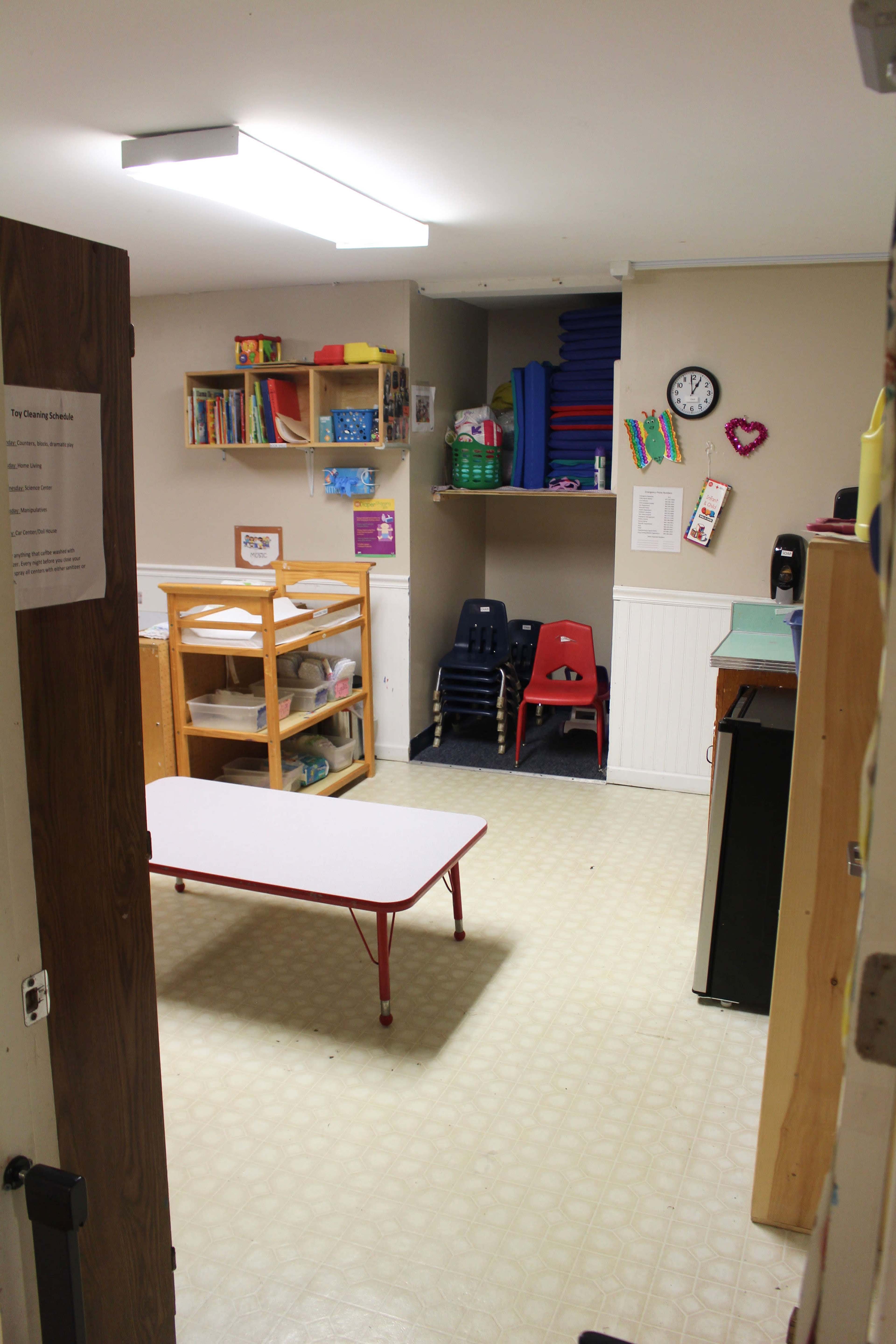 A brightly lit room with shelves, a table, and chairs, designed for a classroom or play area.