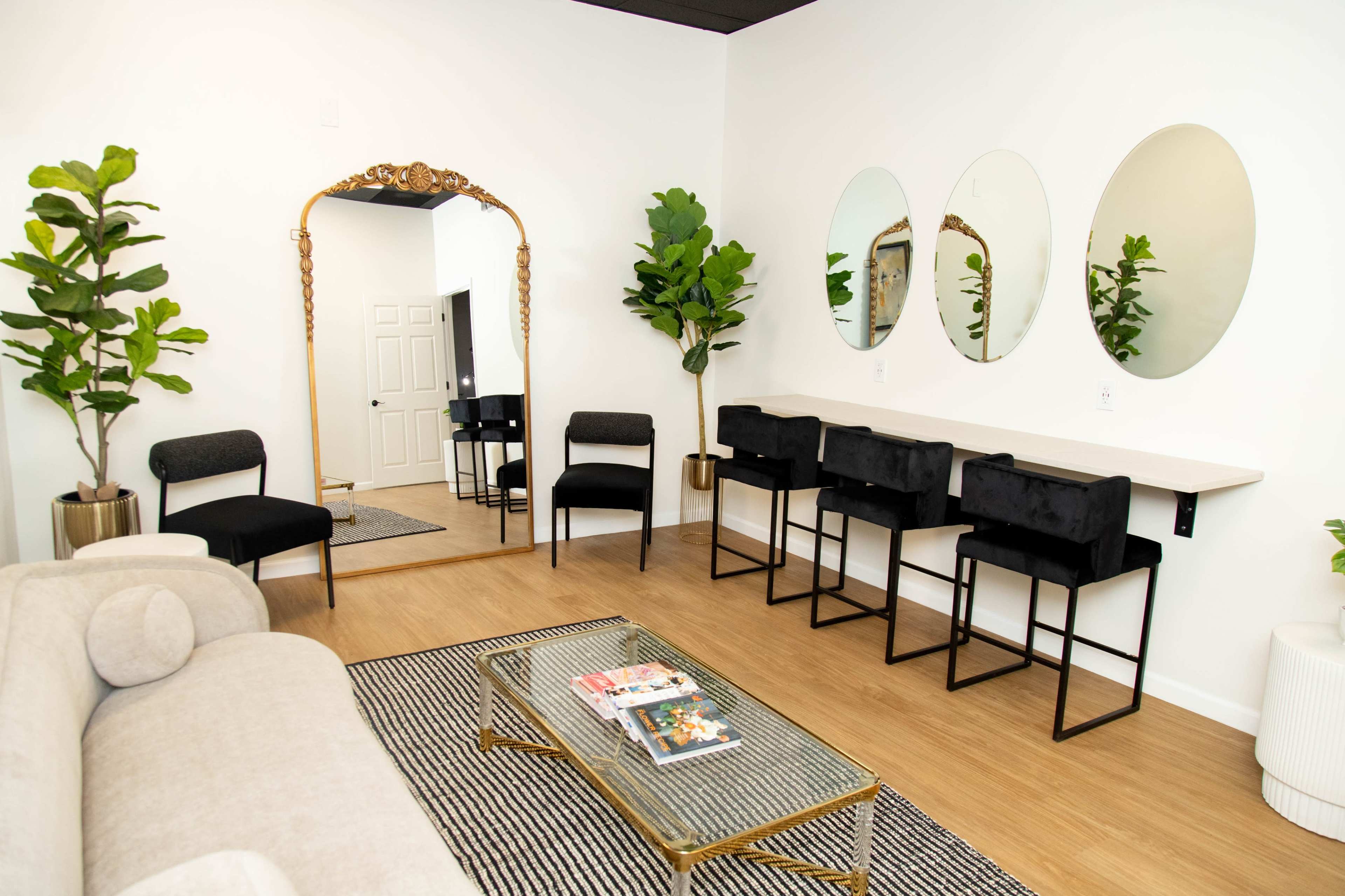 The image shows a modern living space with a beige sofa, a large mirror, three round mirrors on the wall, and a bar area with black stools against a white wall.