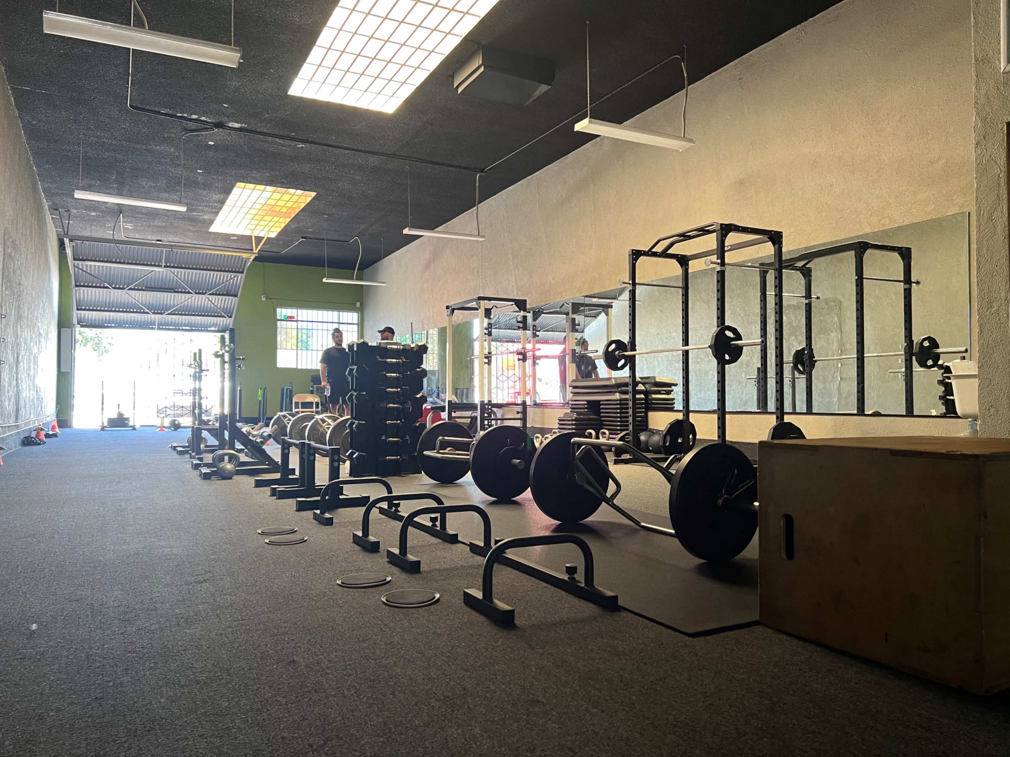 The image shows a fitness gym with various weightlifting equipment, including barbells and benches, lined along a carpeted floor.