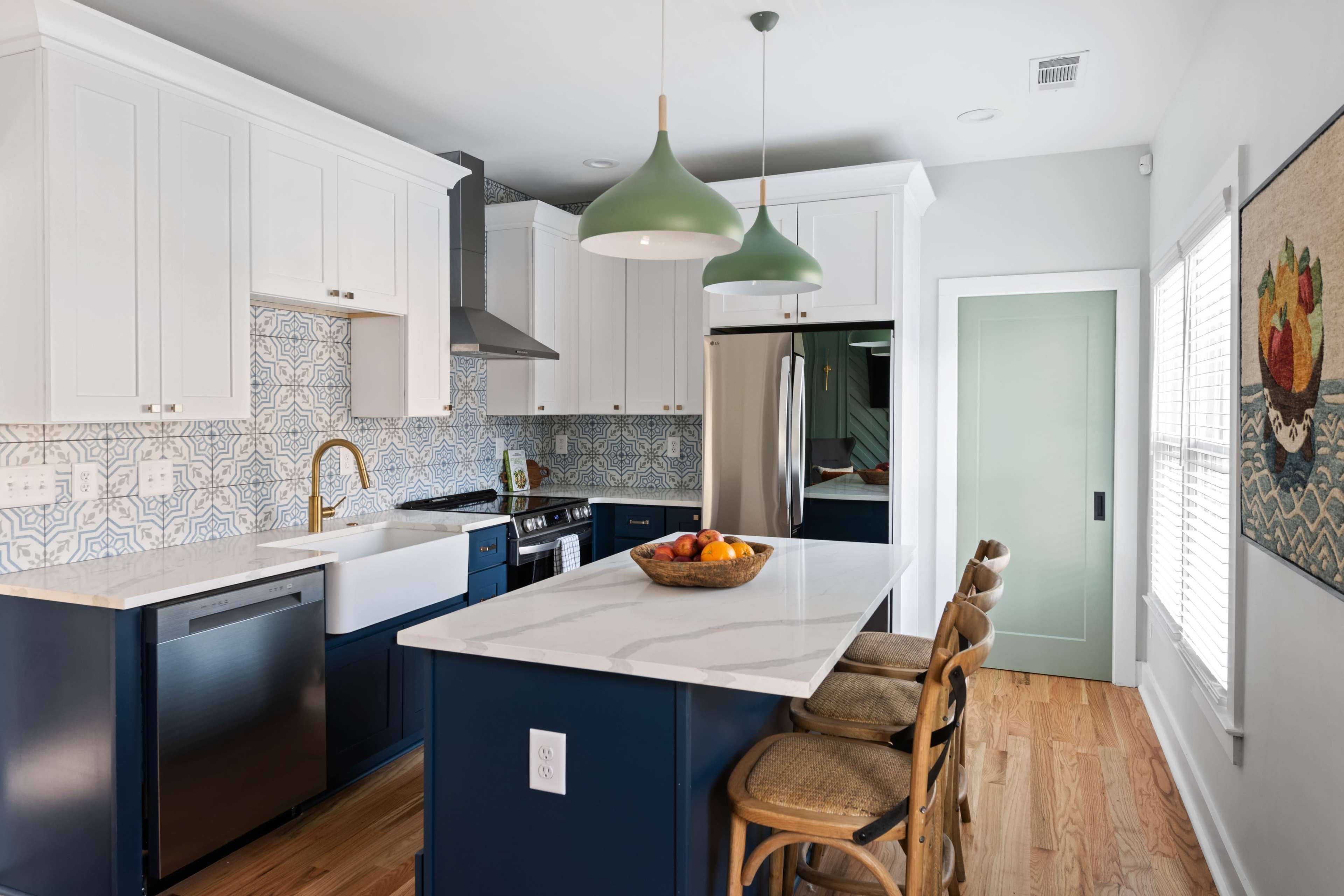 A modern kitchen features white cabinetry, a blue island with seating, and decorative tile backsplash.