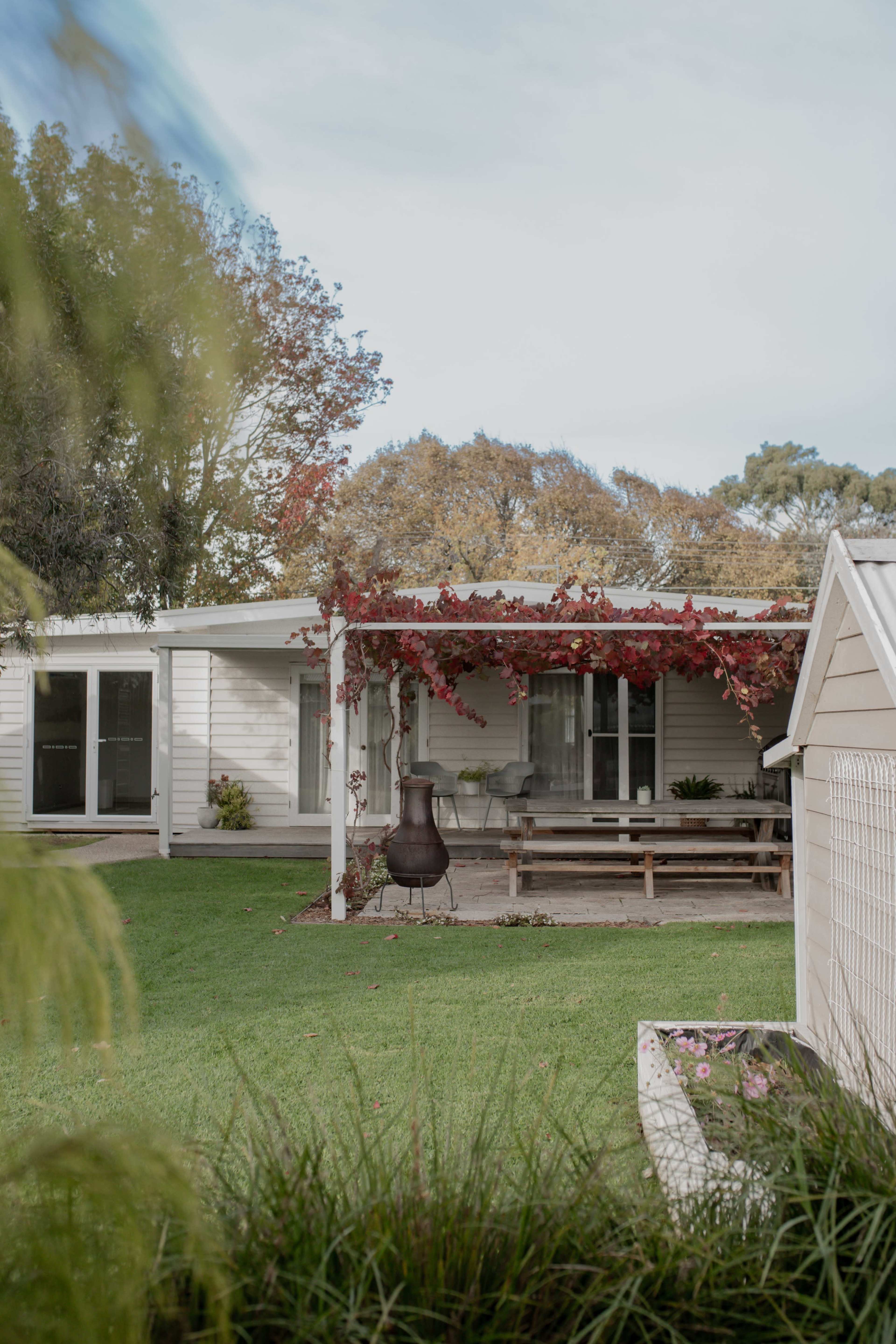 A modern house with a covered patio, surrounded by greenery and autumn foliage.