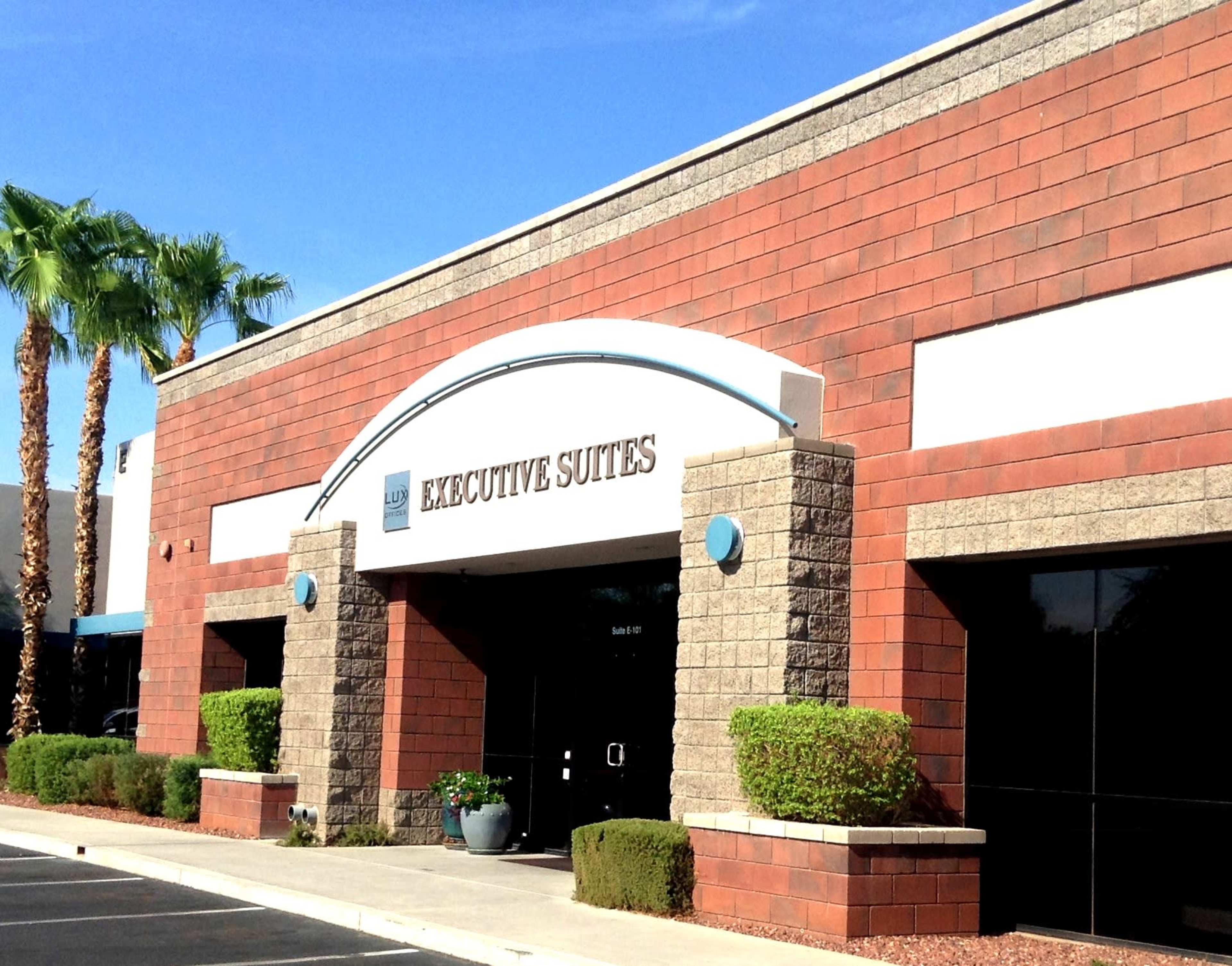 The exterior of a commercial building labeled "EXECUTIVE SUITES" with desert landscaping and palm trees in front.