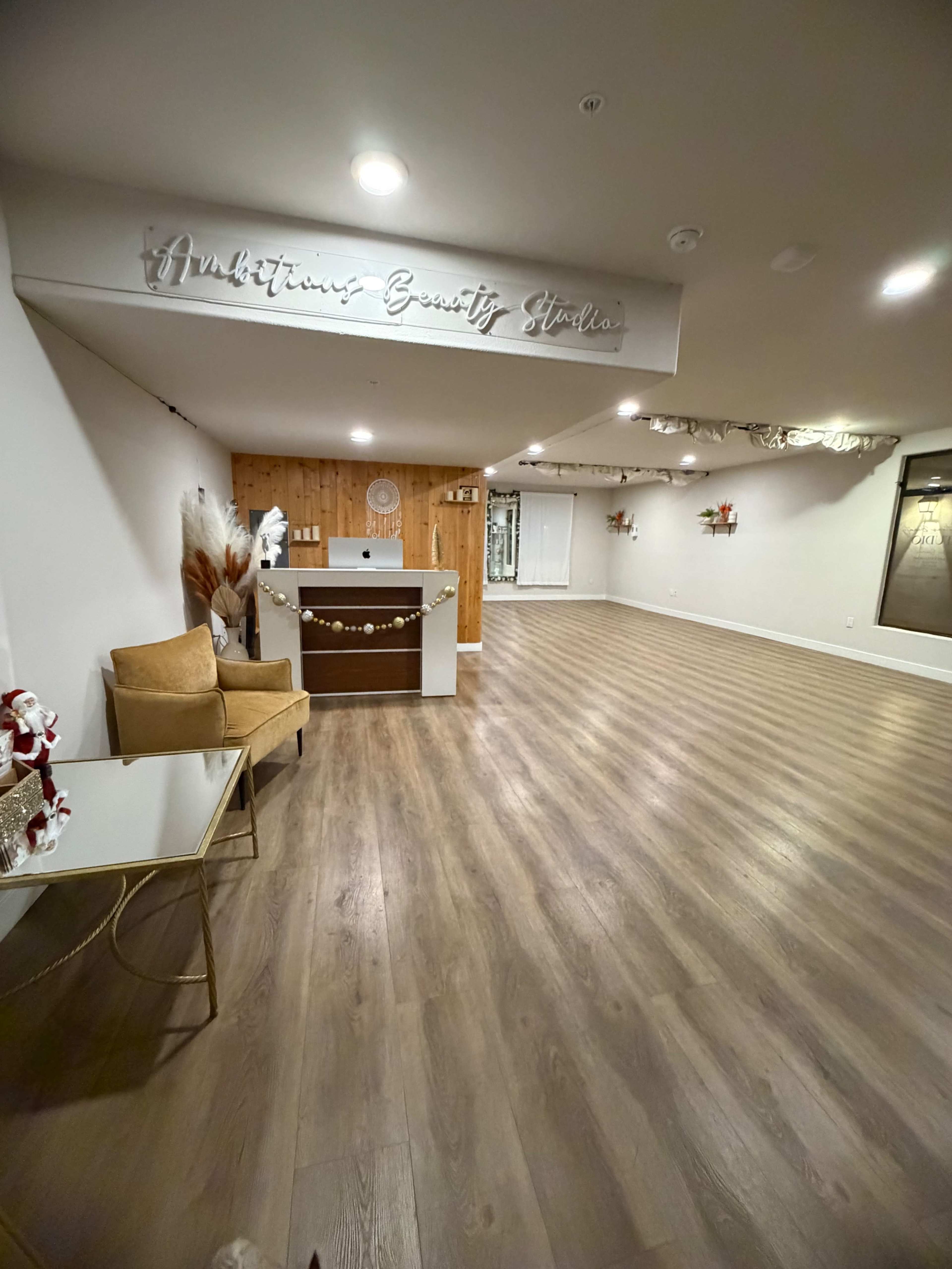The image shows a spacious beauty studio with a reception area featuring a wooden wall, a front desk, and minimal decorations.