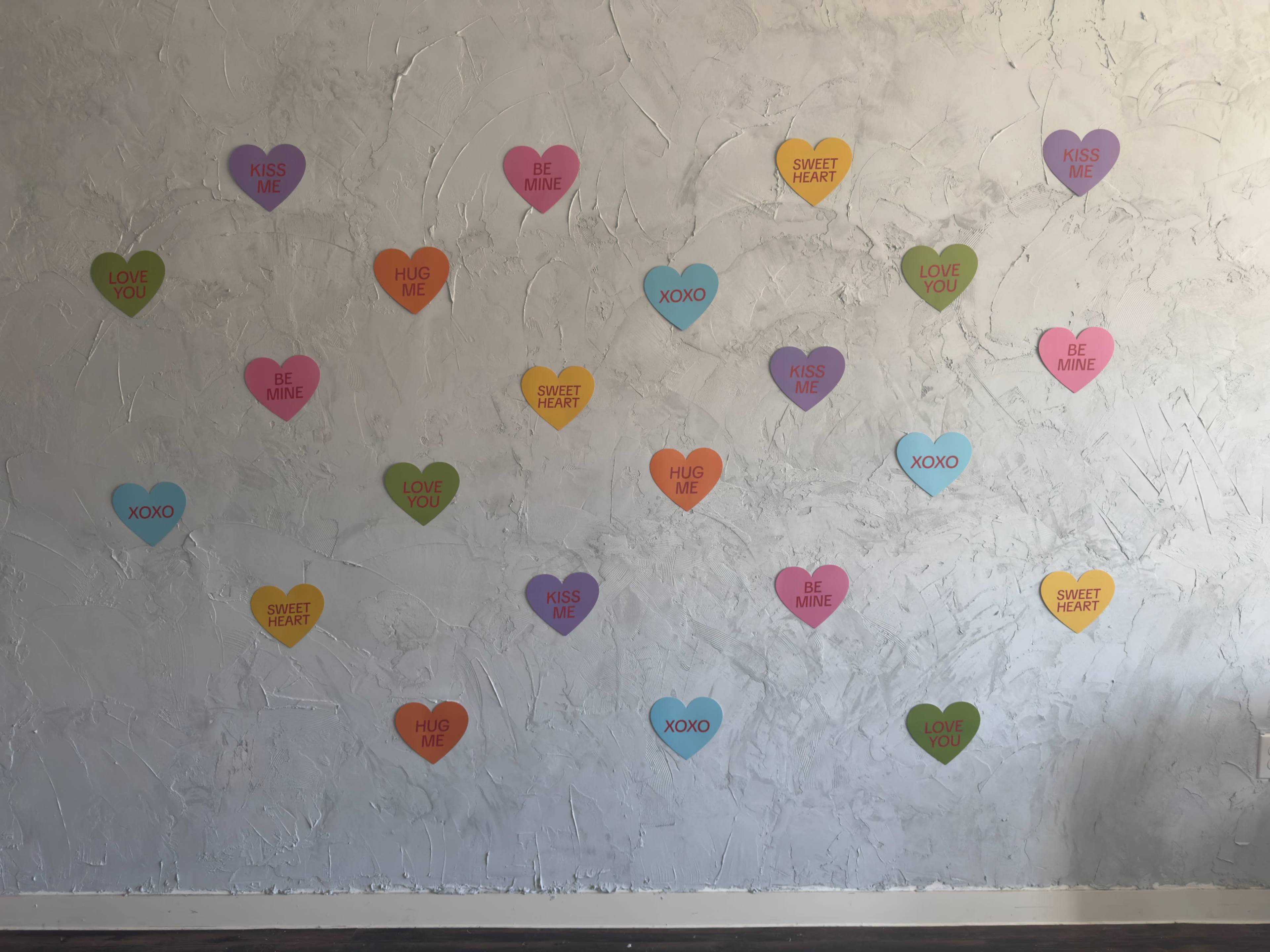 A wall is decorated with colorful heart-shaped stickers featuring various romantic phrases.