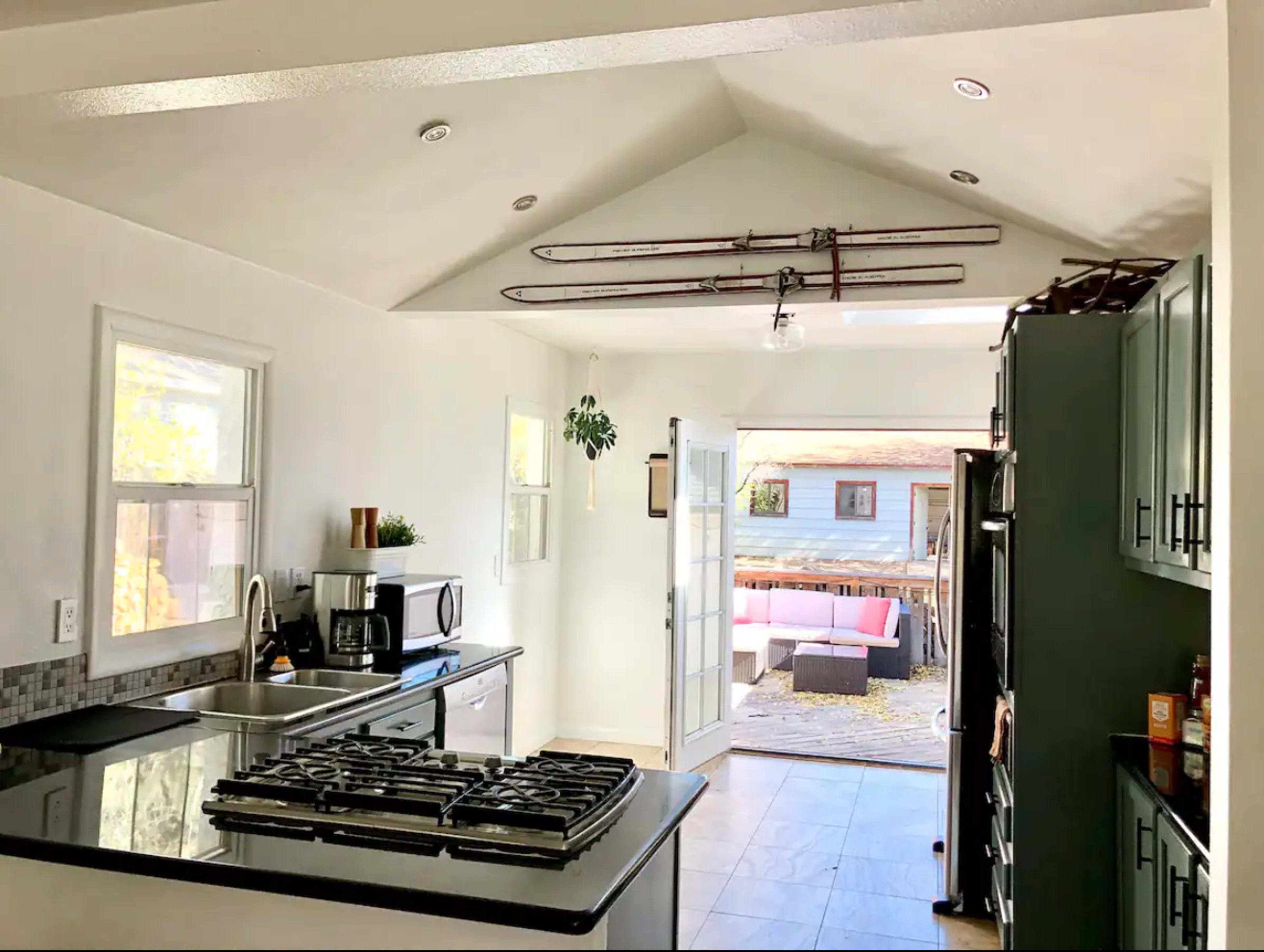 A modern kitchen features a black countertop island and opens into a backyard patio area with ski equipment displayed on the ceiling.