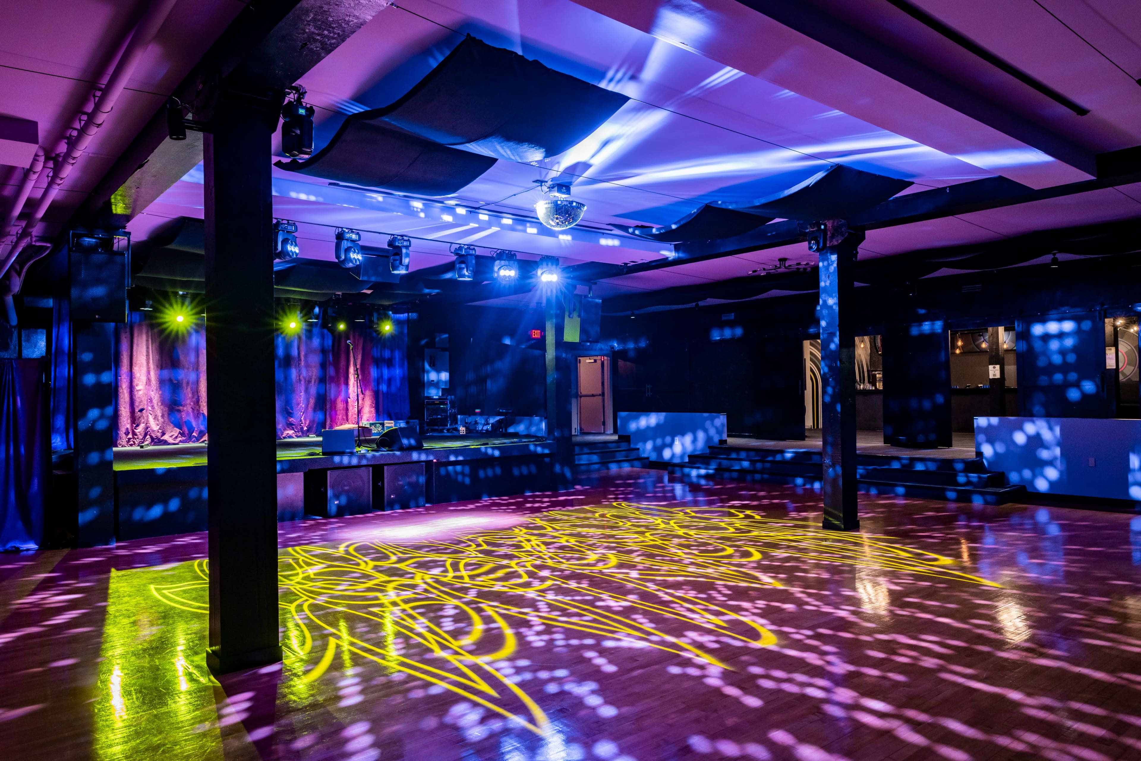 The image shows an empty entertainment venue with colorful lights projecting various patterns onto the dance floor.