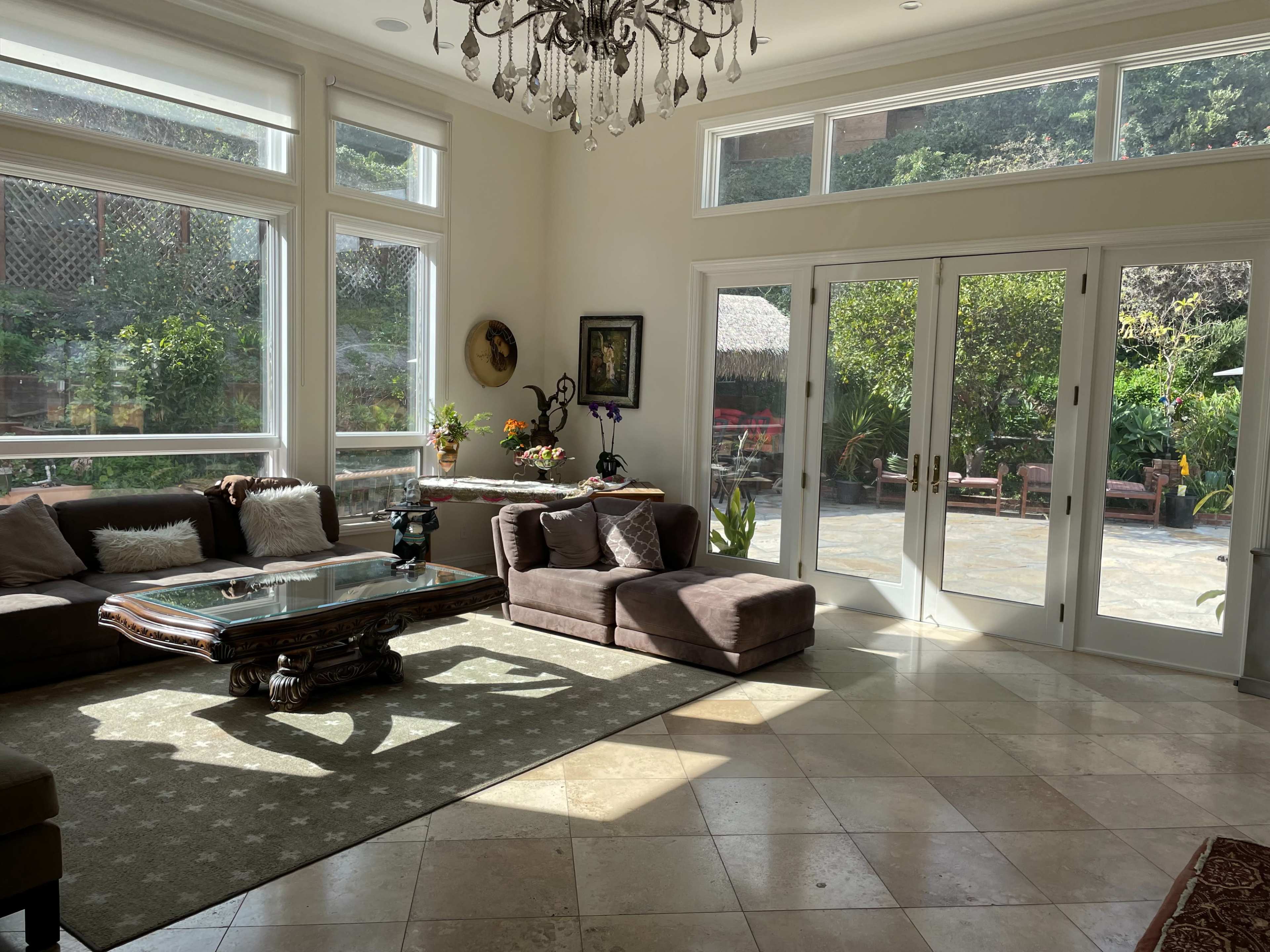 The spacious living room features a large sofa, a glass-topped coffee table, and abundant natural light streaming through large windows.