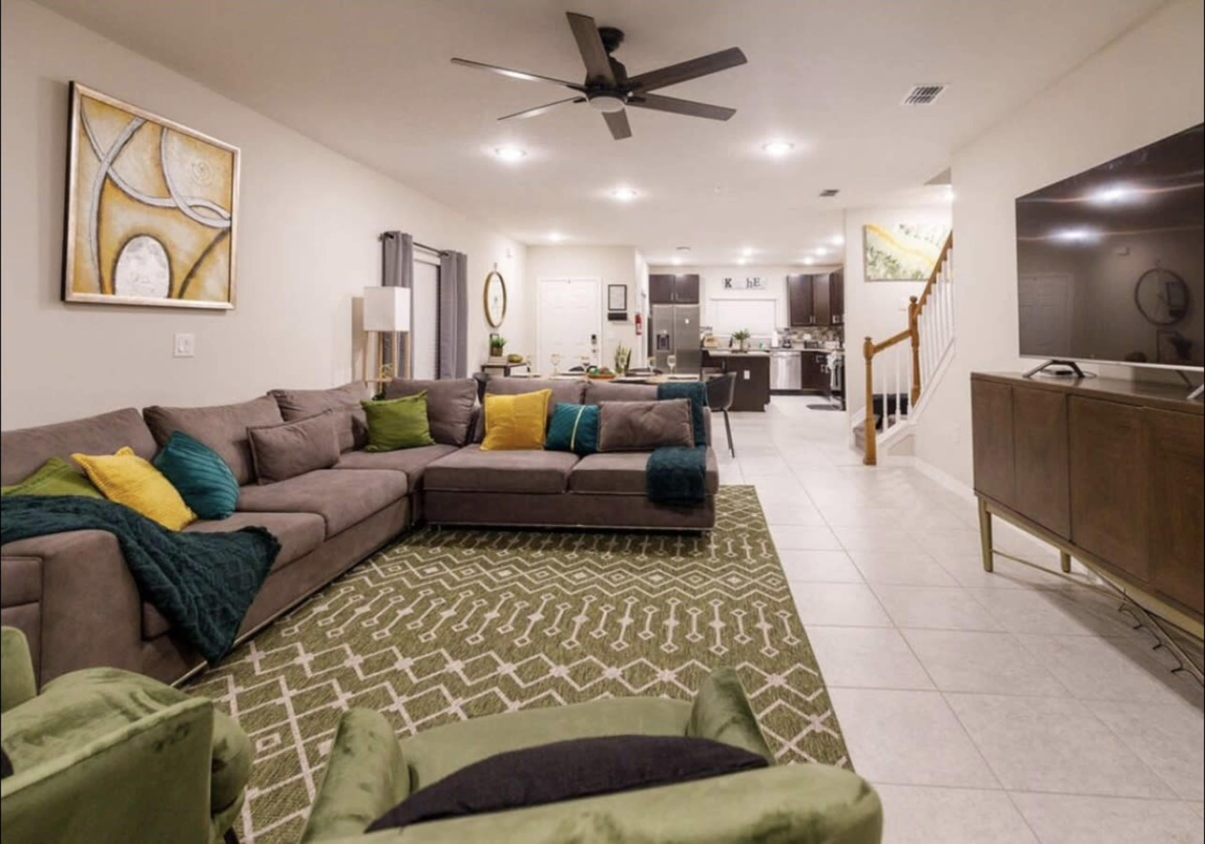 A modern living room with a sectional sofa, an area rug, and a spacious layout leading to a kitchen area in a well-lit home.