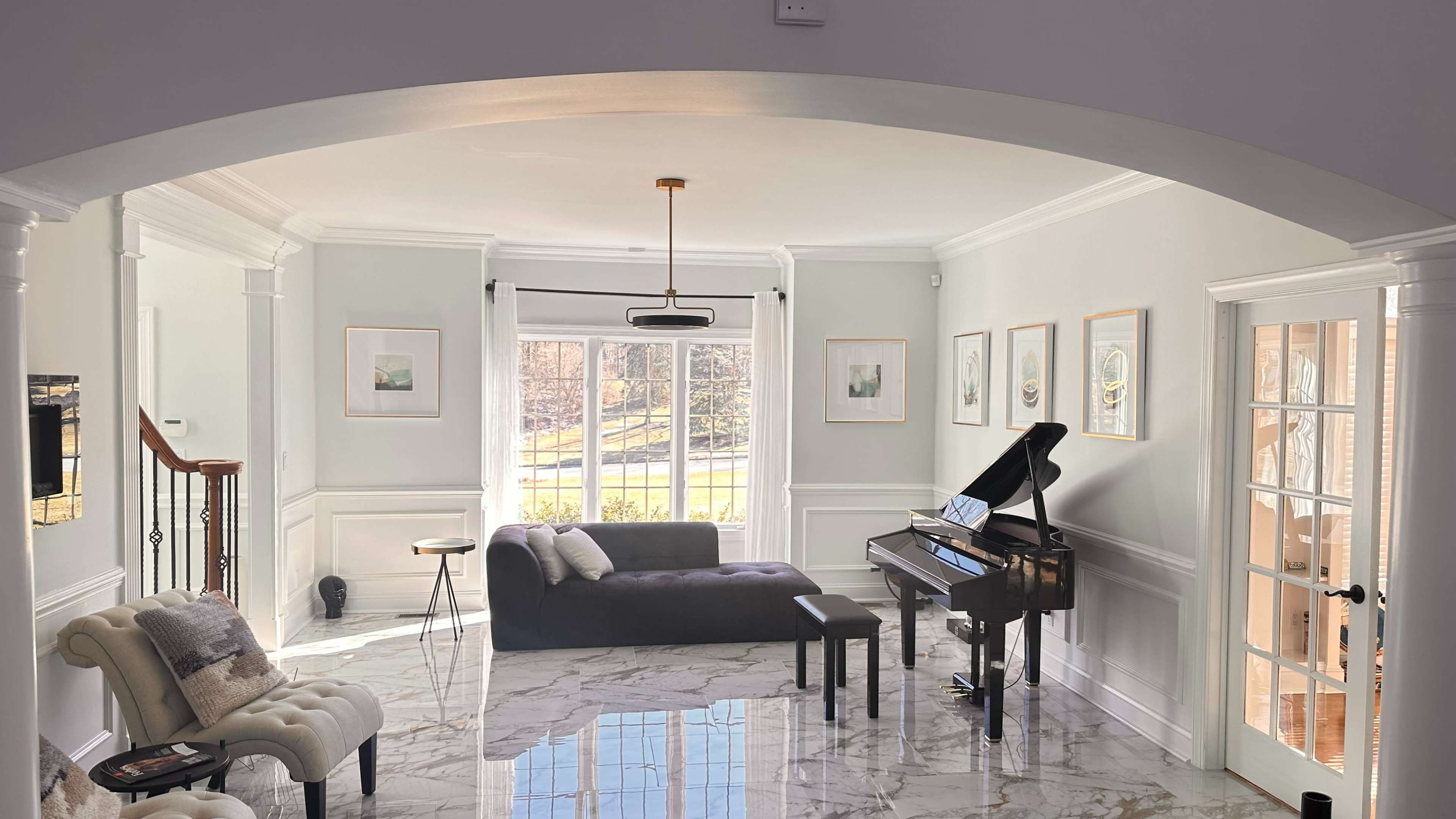 A bright living room featuring a black piano, a gray sofa, and marble flooring with large windows that allow natural light to enter.