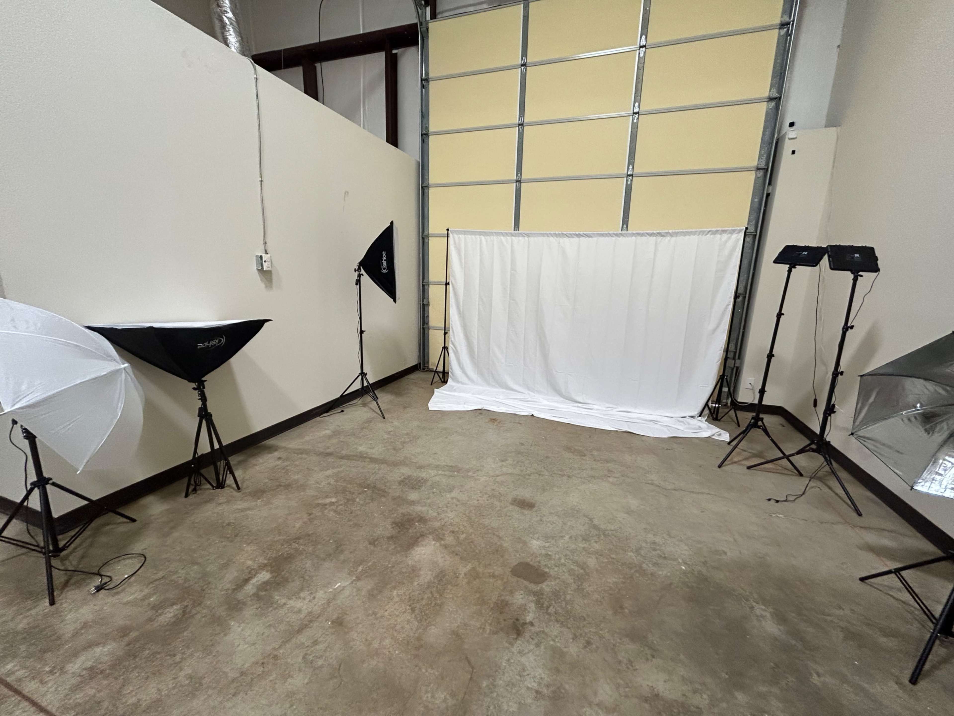 The image shows a photography studio with a white backdrop set up in the center, flanked by multiple lighting equipment on stands.
