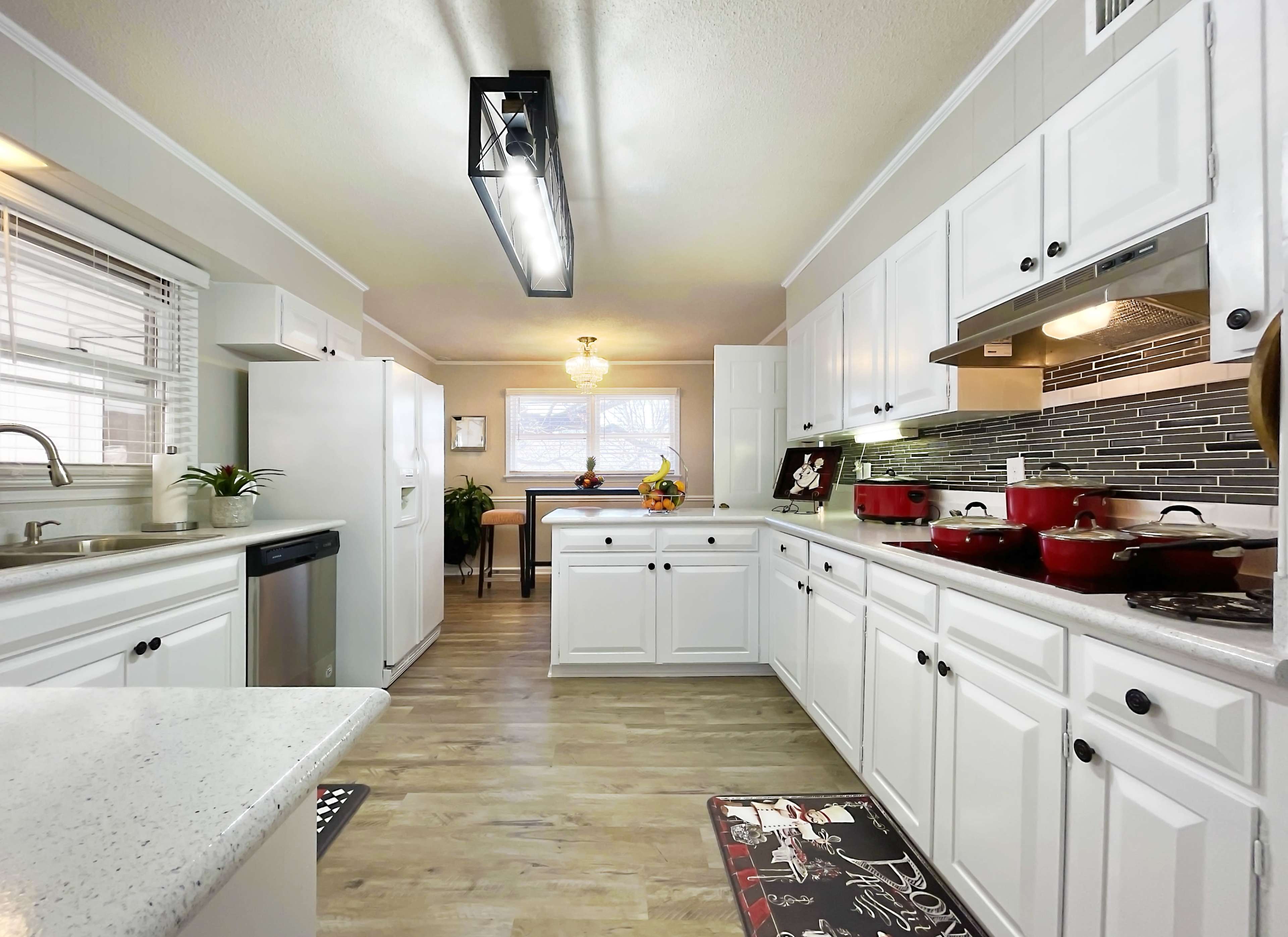 A bright kitchen with white cabinets, stainless steel appliances, and a central island featuring a sink, along with red cookware on the countertops.