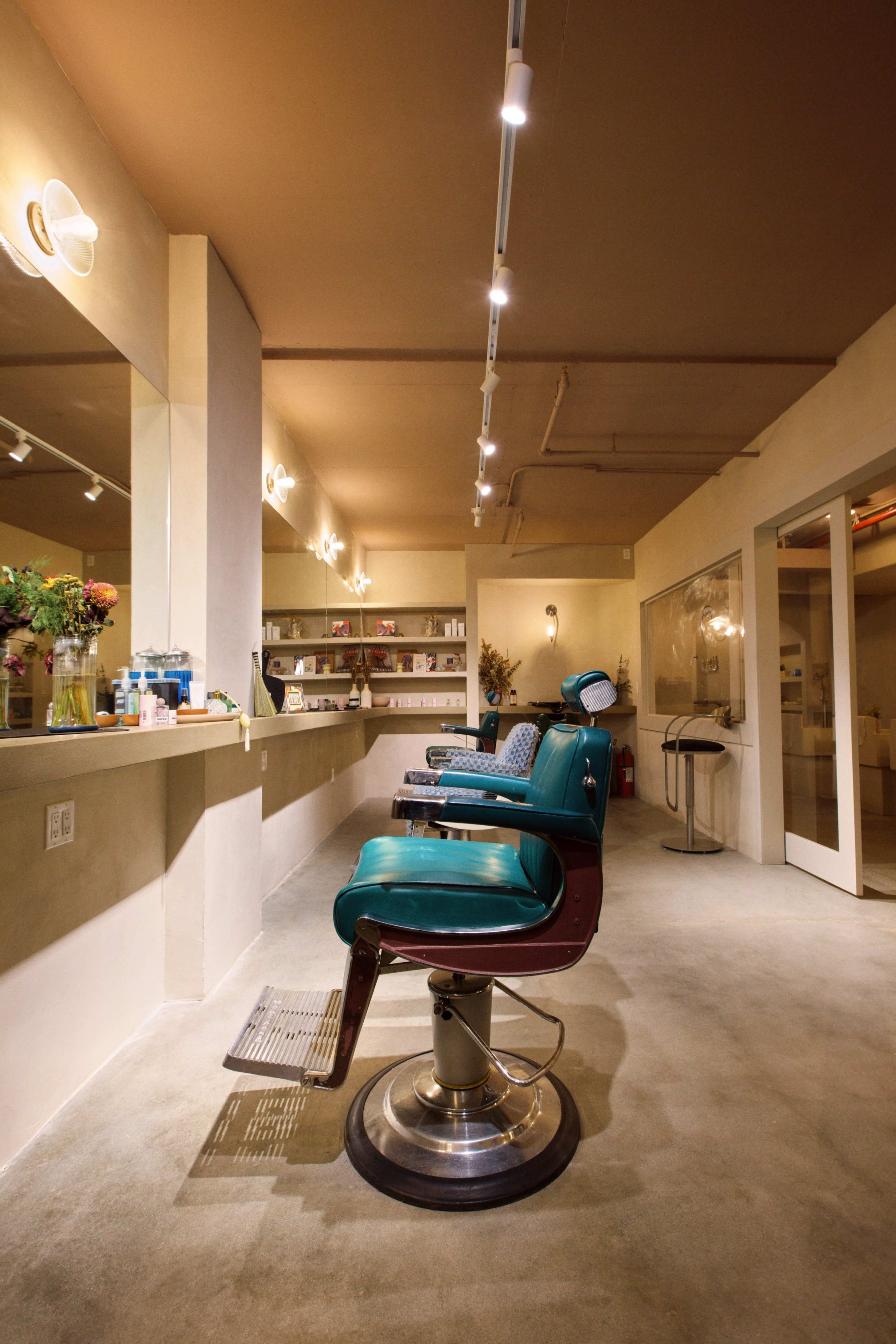 The image shows a modern barber shop interior with two barber chairs and a well-lit, minimalist design.