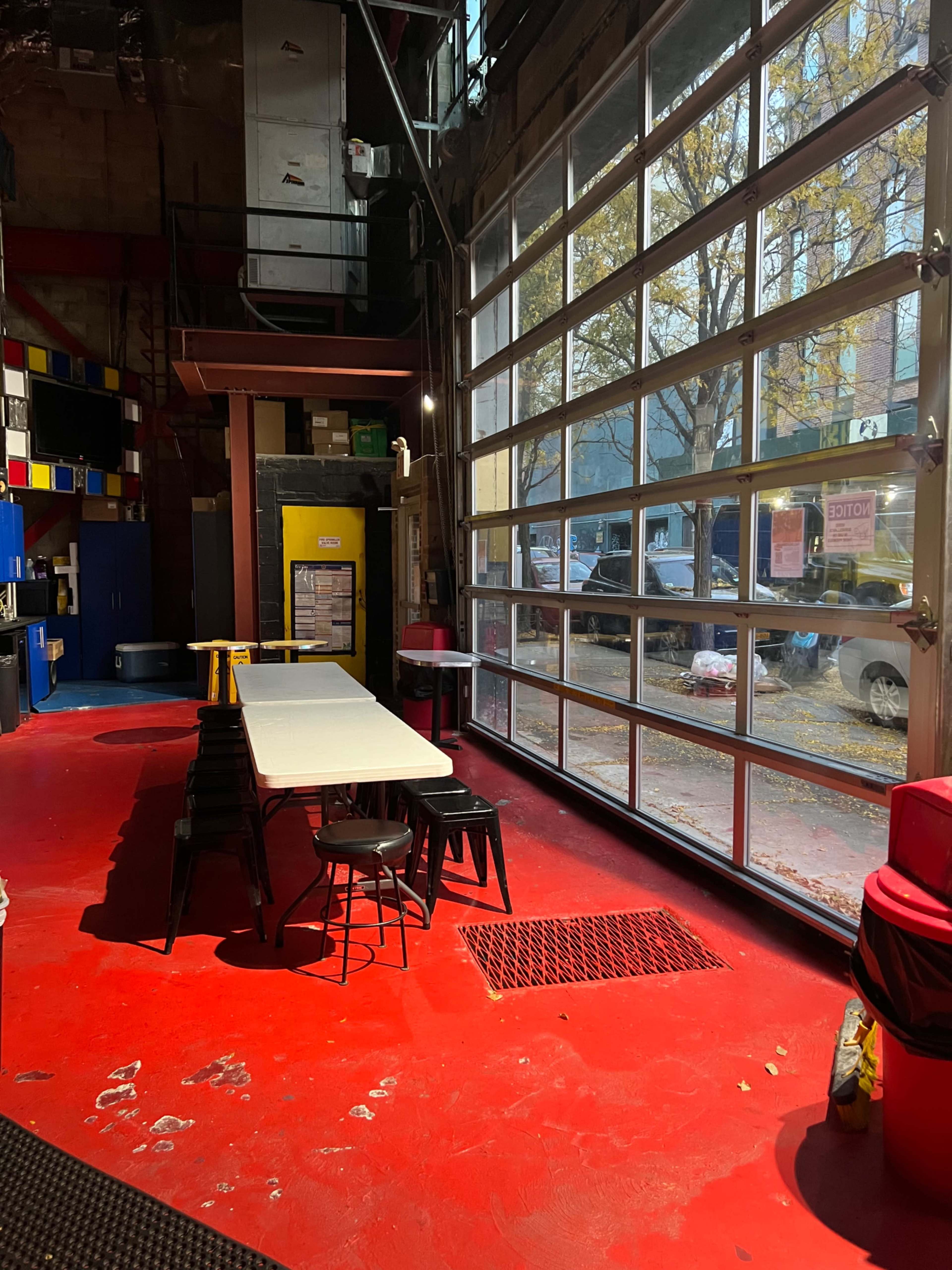 The scene shows an industrial-style room with a long white table and black chairs, large glass windows letting in natural light, and a red floor.