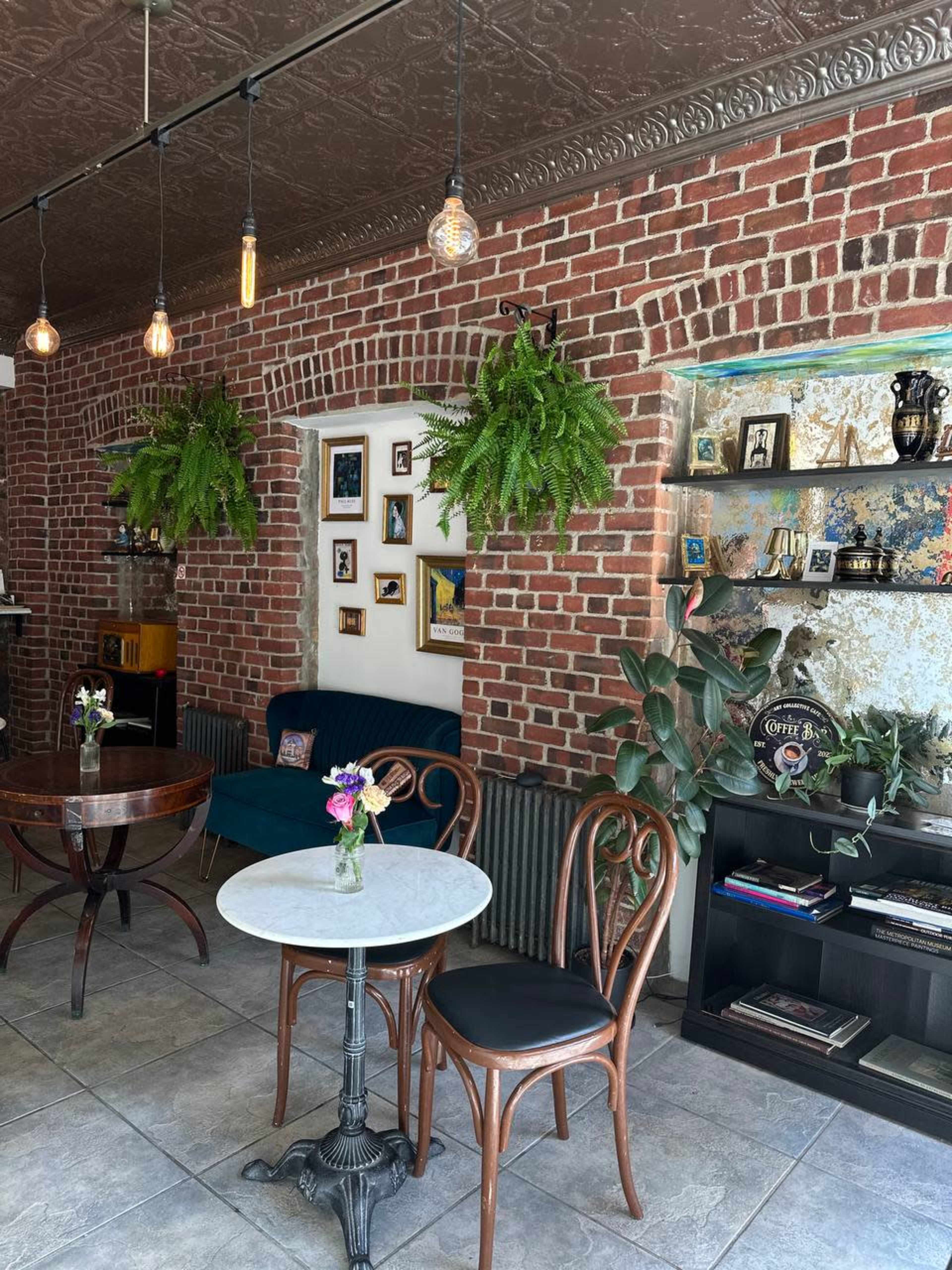A cozy café interior with exposed brick walls, hanging plants, and a mix of furniture including a round marble table and wooden chairs.