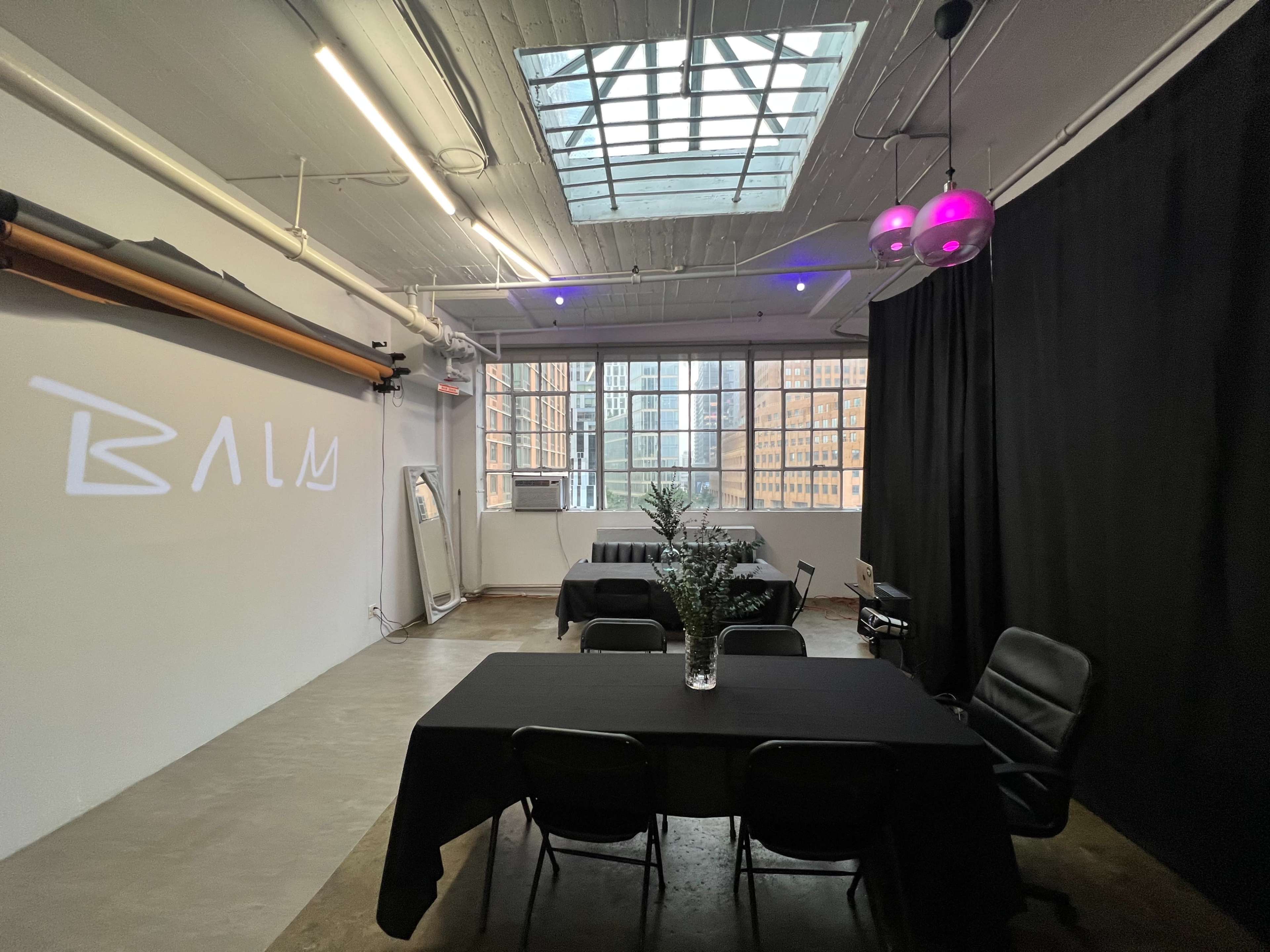 A spacious interior with black tables and chairs, a plant centerpiece, and large windows displaying a cityscape.