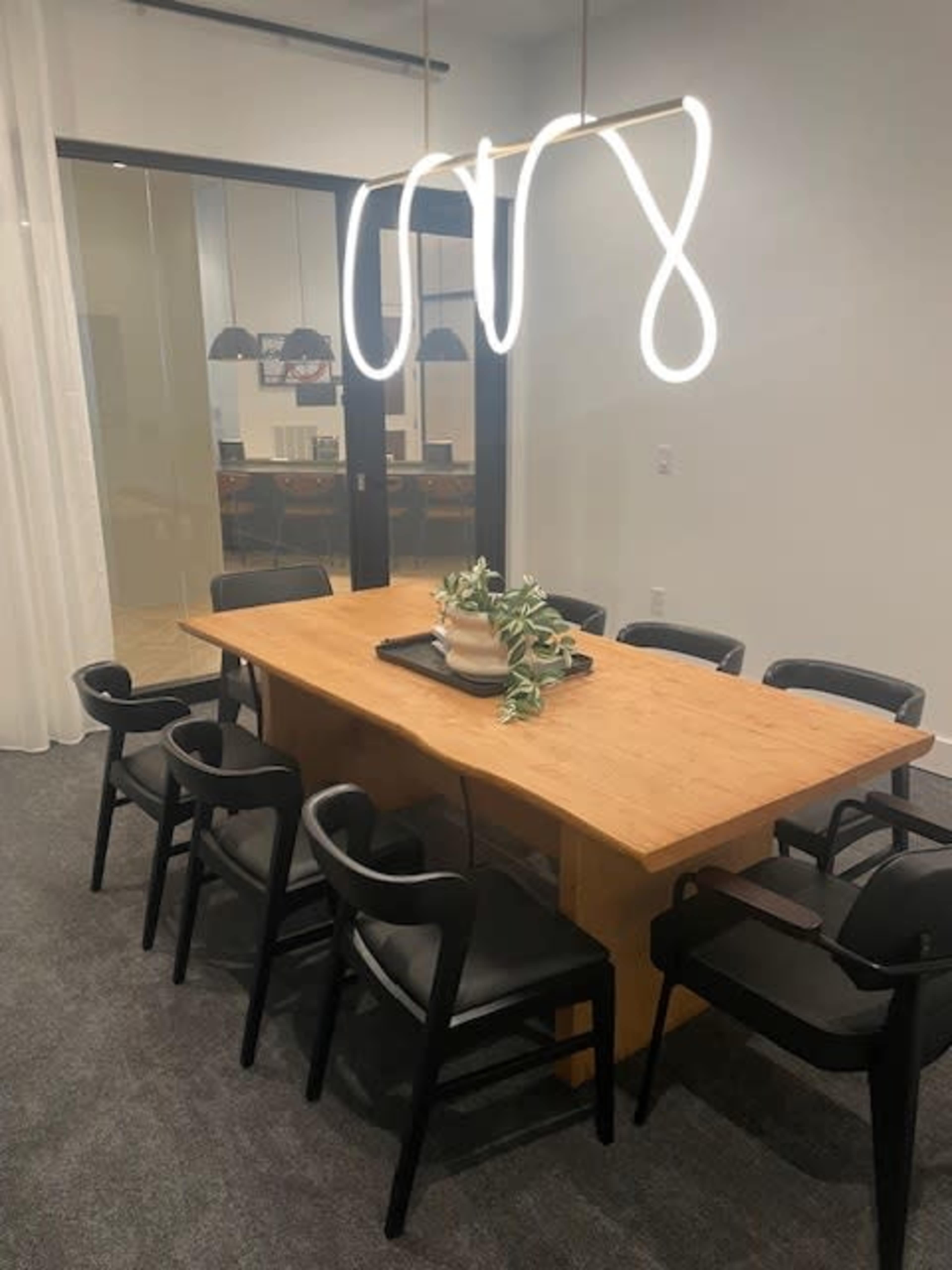 A wooden dining table is surrounded by black chairs under a modern light fixture in a well-lit dining area.