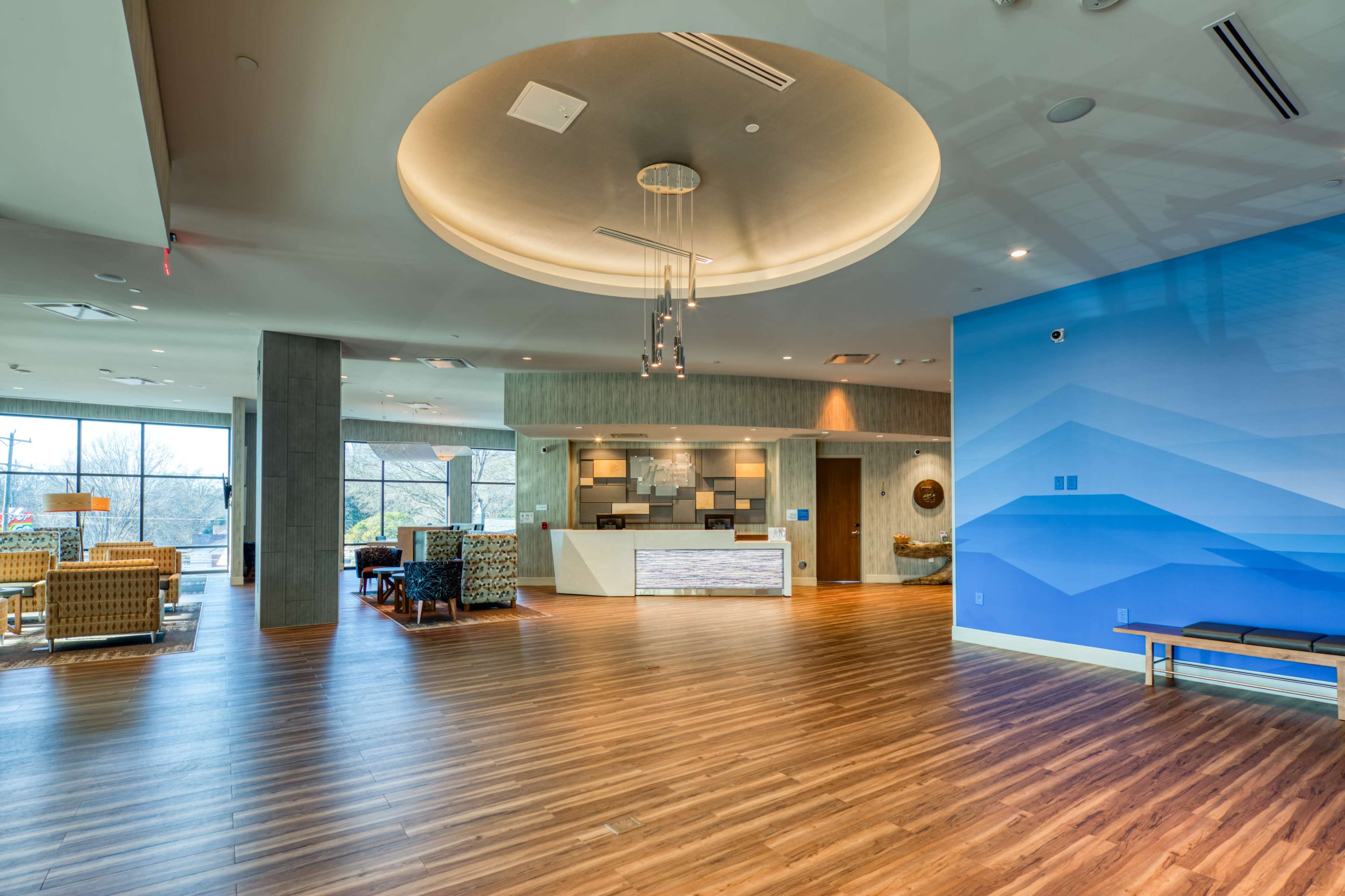The image shows a modern lobby area with a reception desk, seating arrangements, and large windows allowing natural light.