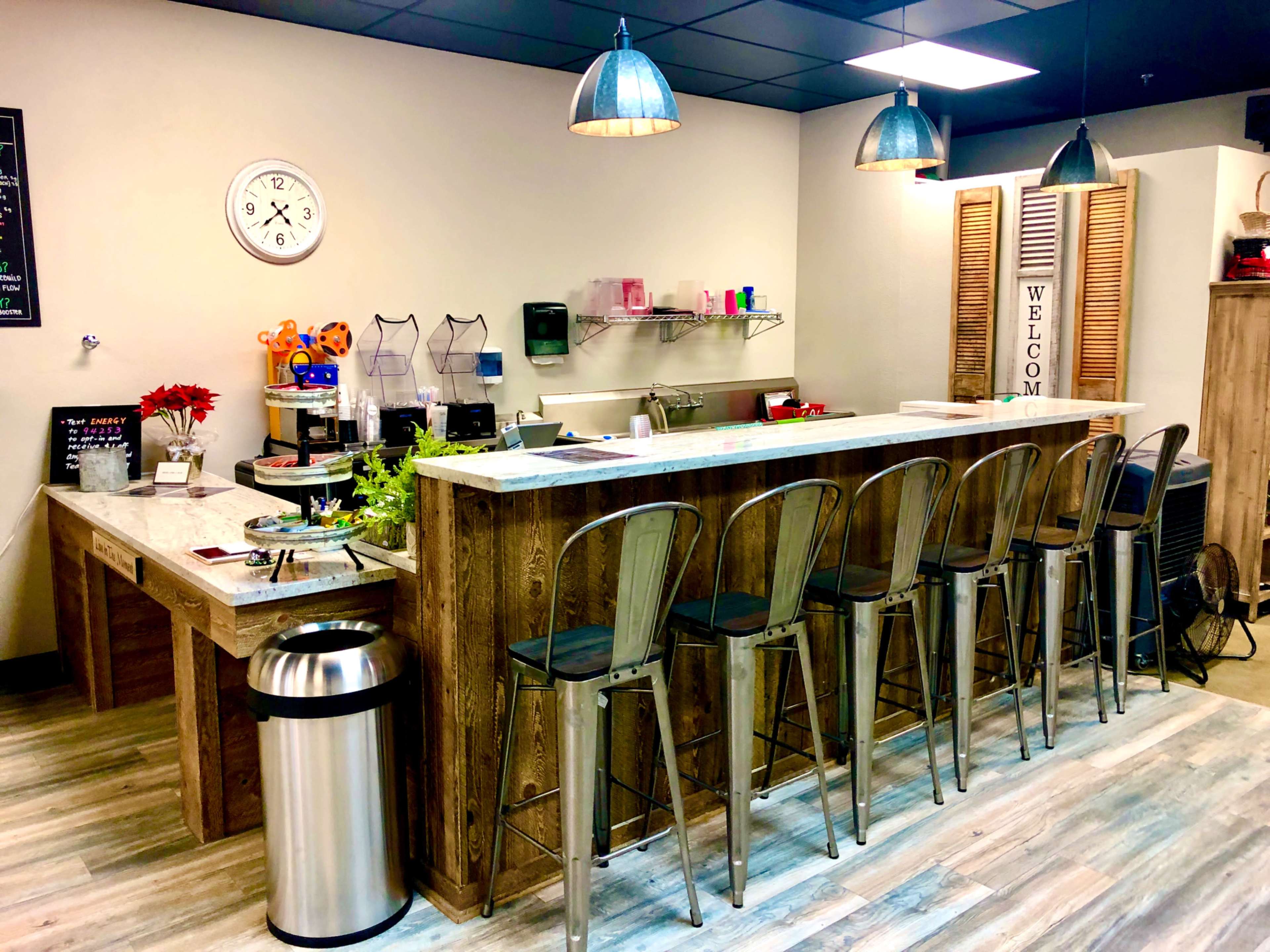 A modern café interior featuring a wooden counter with high stools, a clock on the wall, and various kitchen items arranged on the counter.
