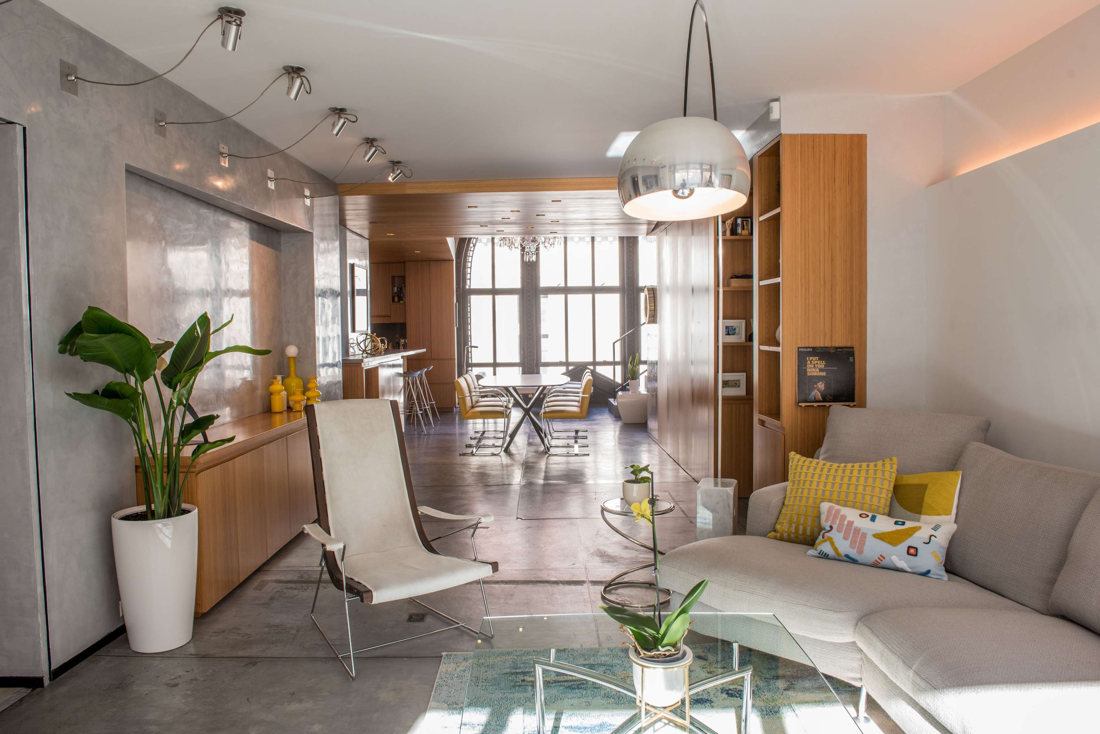 A contemporary living space featuring a light-colored sectional sofa, a glass coffee table, and an open layout that connects to a dining area with modern furnishings.