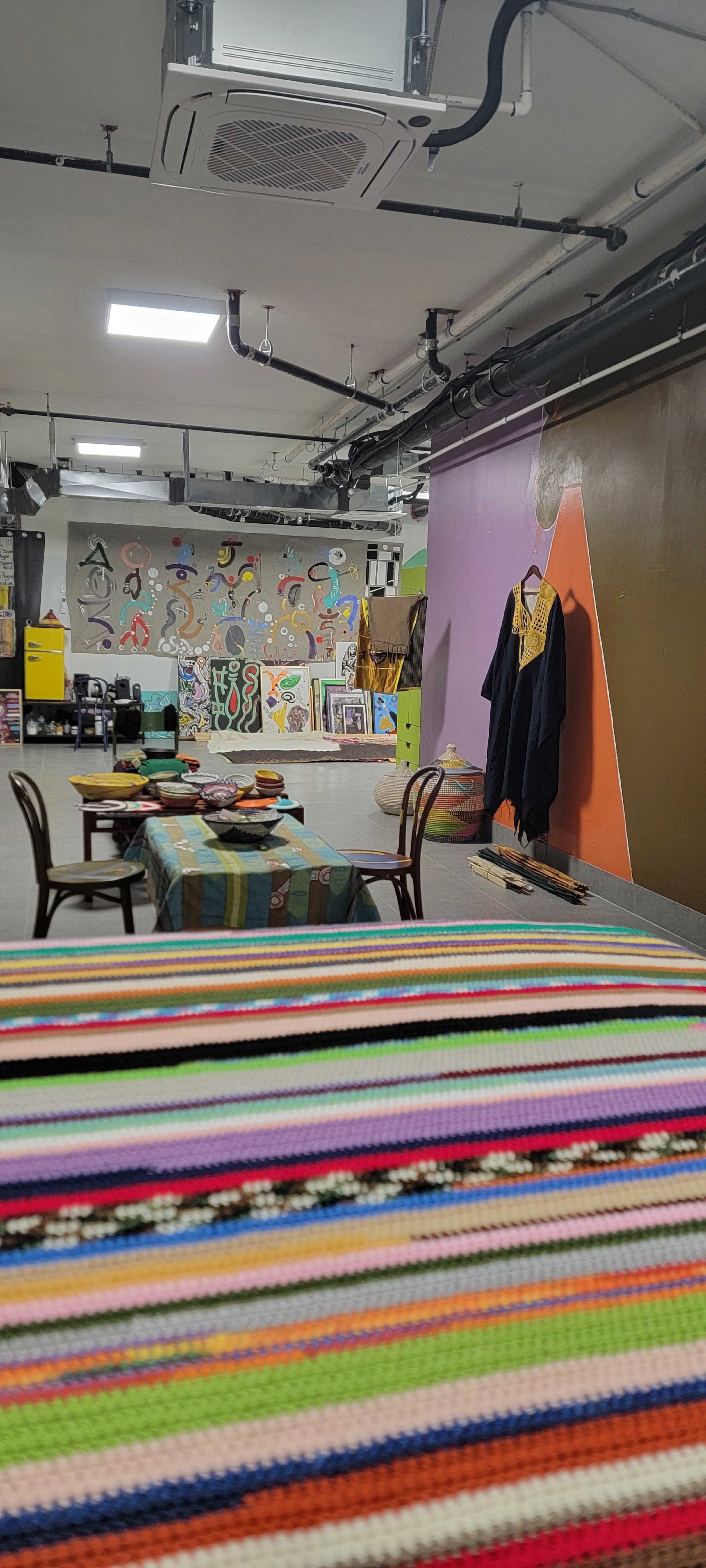 The image shows a creative workspace featuring colorful murals on the walls, a table with patterned cloth, and various art supplies arranged around the room.