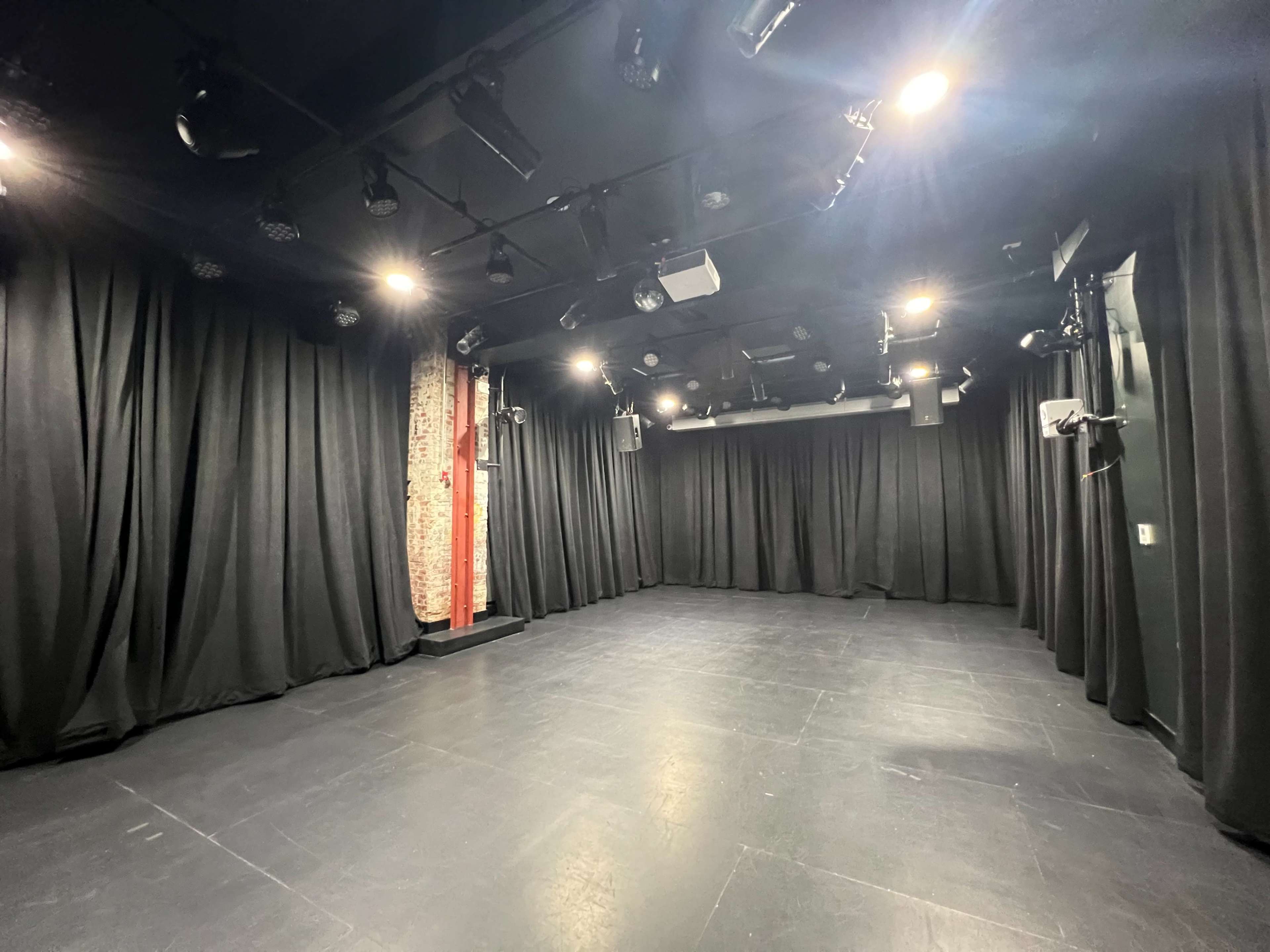 The image shows an empty stage area with black curtains, dim lighting, and a smooth floor.