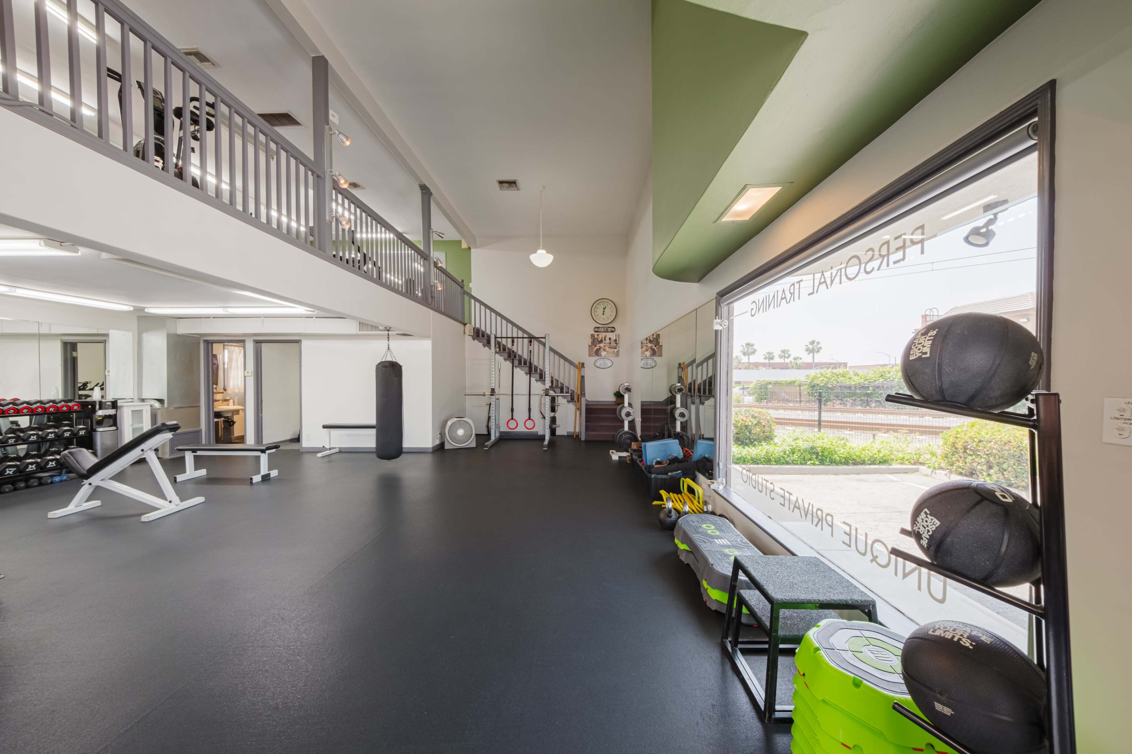 A gym interior with various exercise equipment, including weights and benches, along with a staircase leading to a second level.