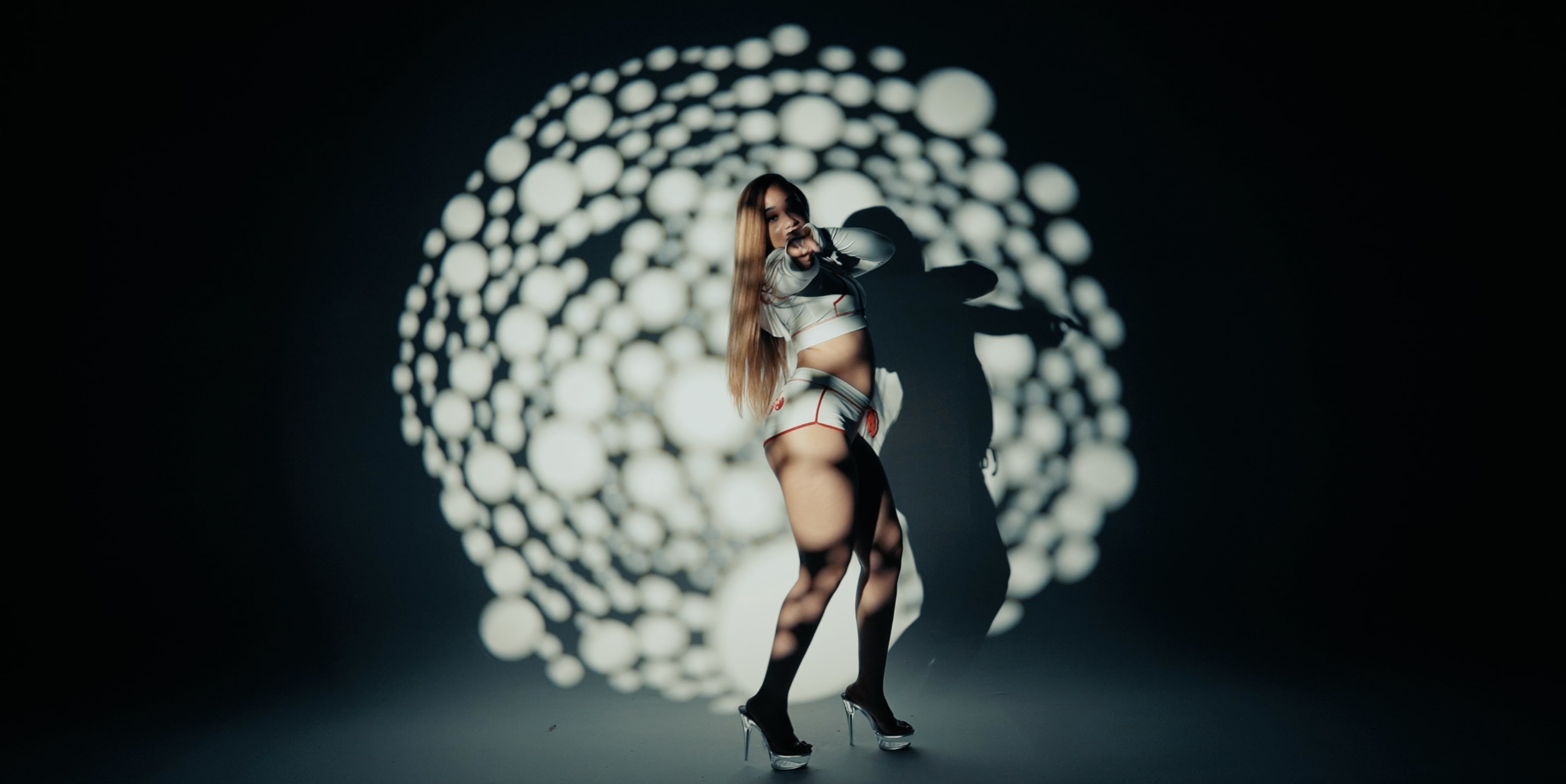 A model stands in front of a dark backdrop with a circular pattern of white light and shadows.