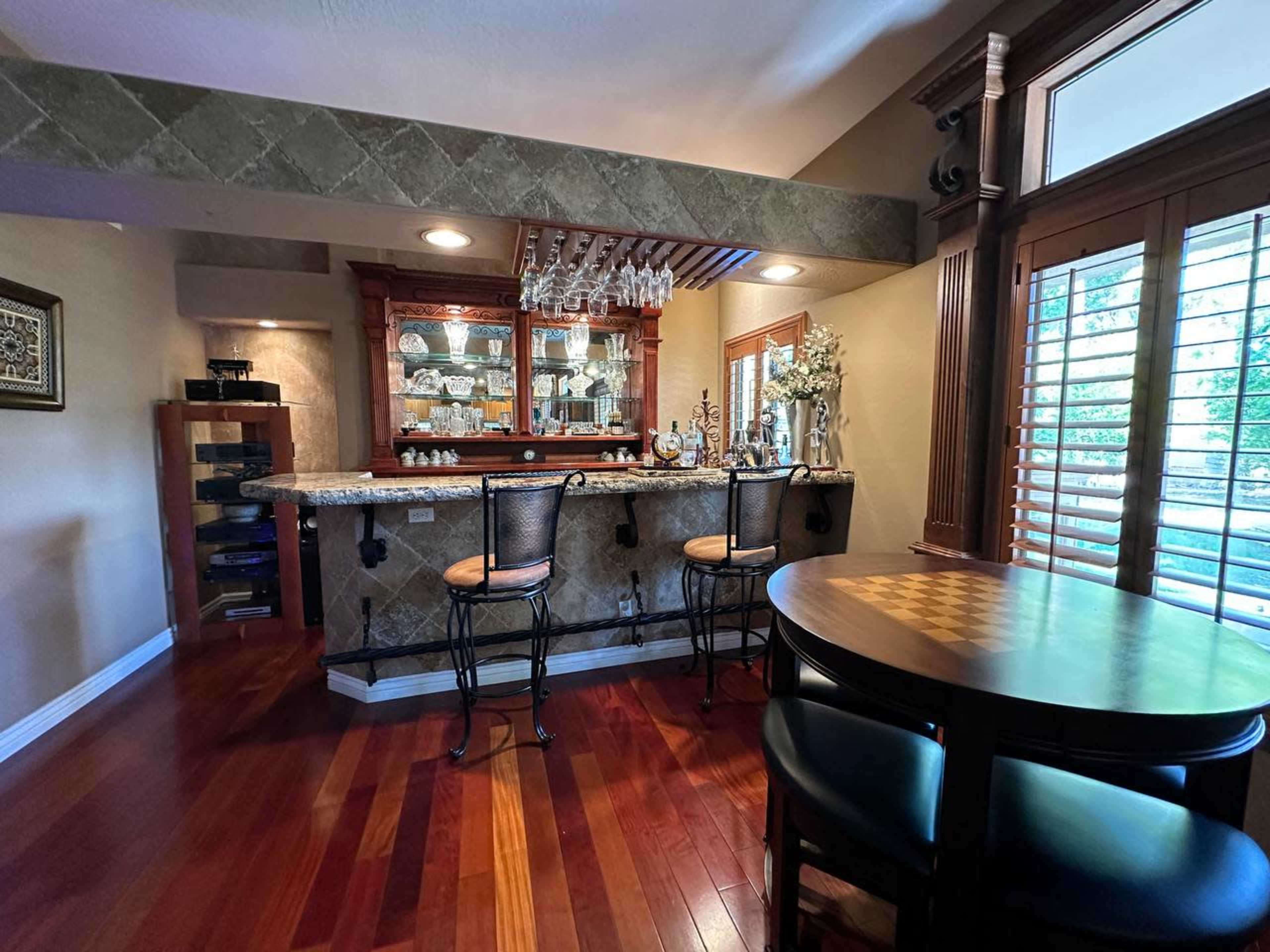 A well-furnished home bar area with a wooden counter, bar stools, and a display of glassware against a decorative backdrop.