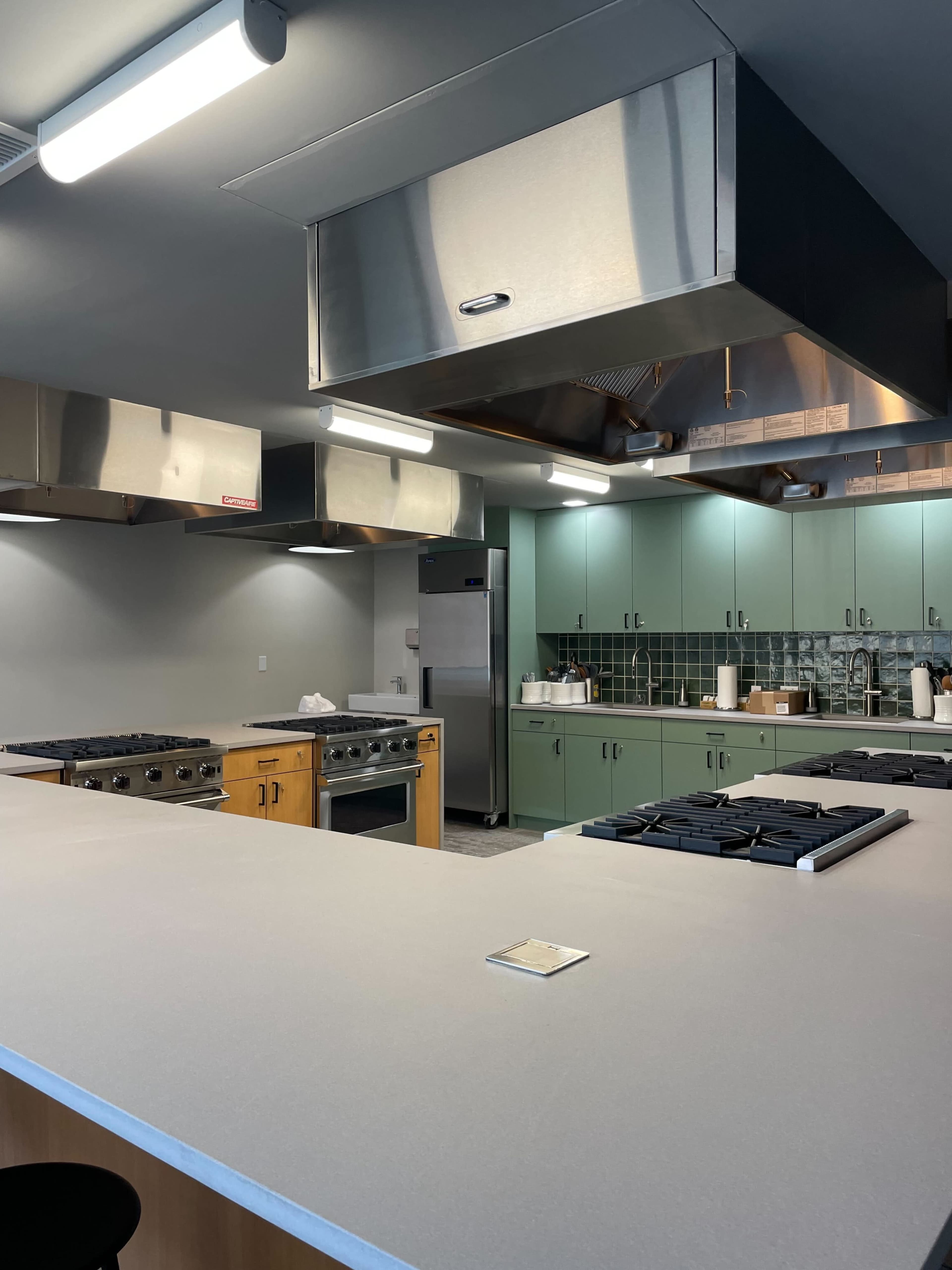 A modern kitchen with multiple cooking stations, stainless steel appliances, and green cabinetry.