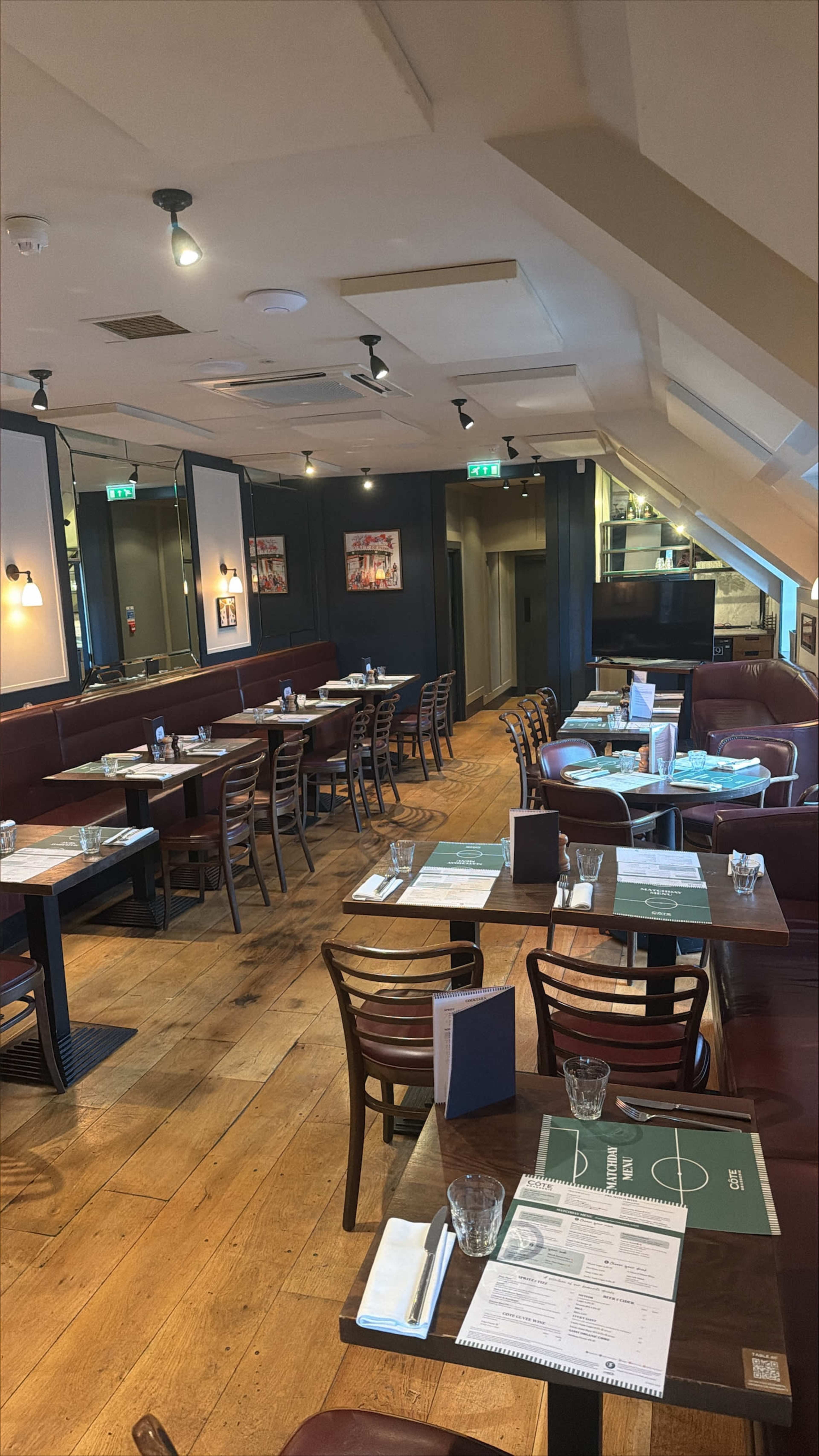 The image shows an interior of a restaurant with wooden floors, several tables set for dining, and booths along the walls.