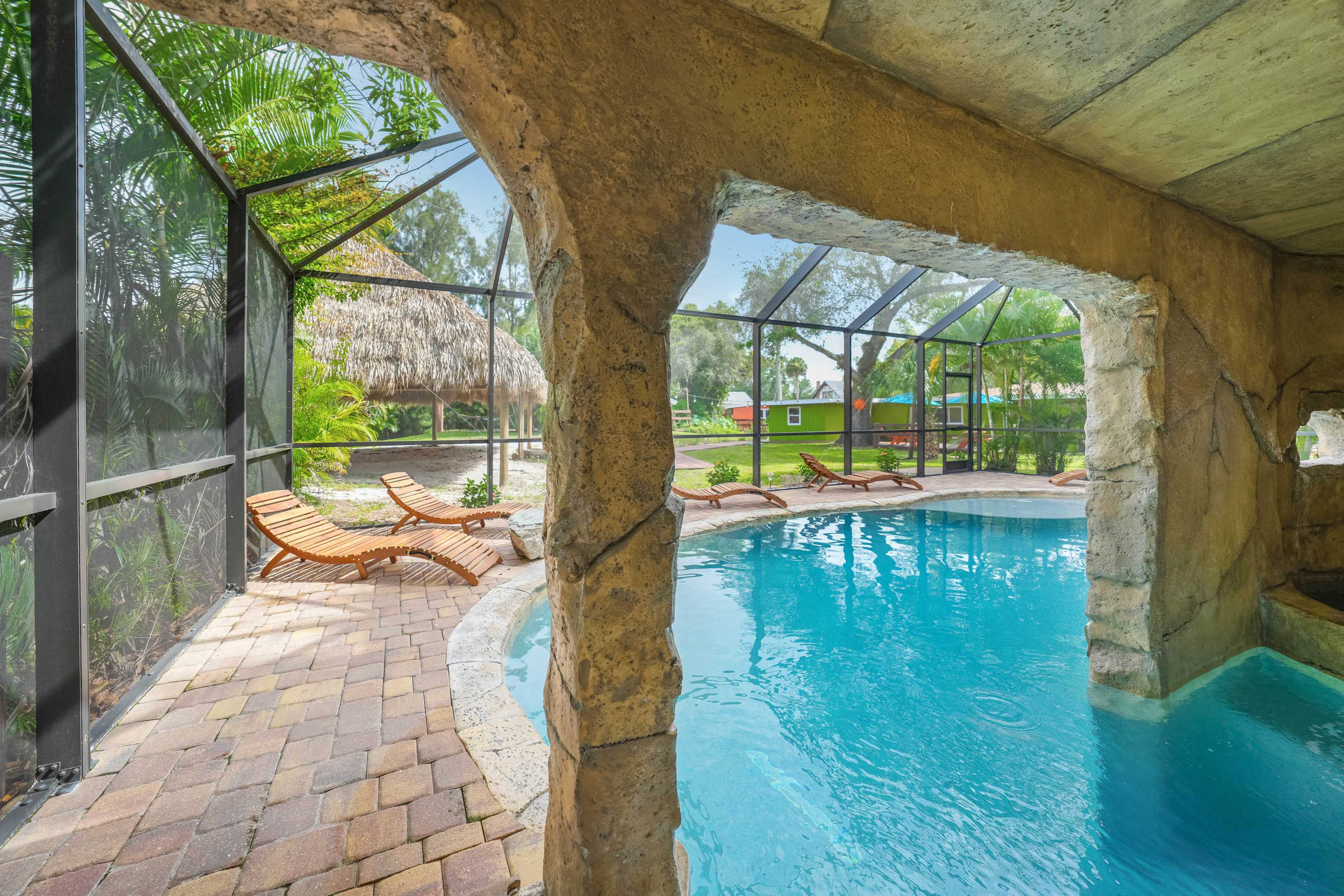 A screened-in pool area with a stone archway, featuring a clear blue pool and lounge chairs arranged around it.