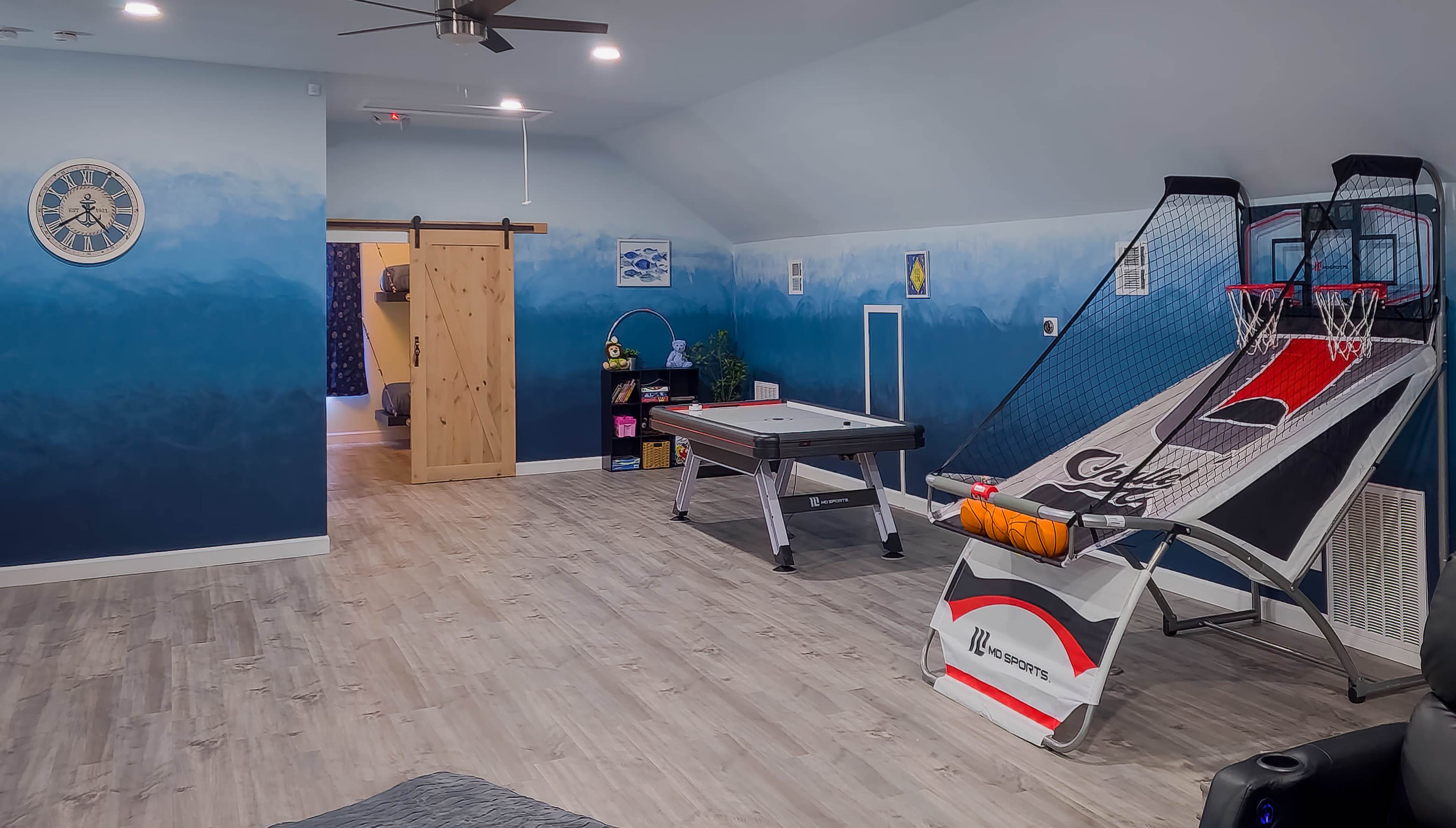 A game room featuring an air hockey table, a basketball shooting game, and a rustic sliding door leading to another space.