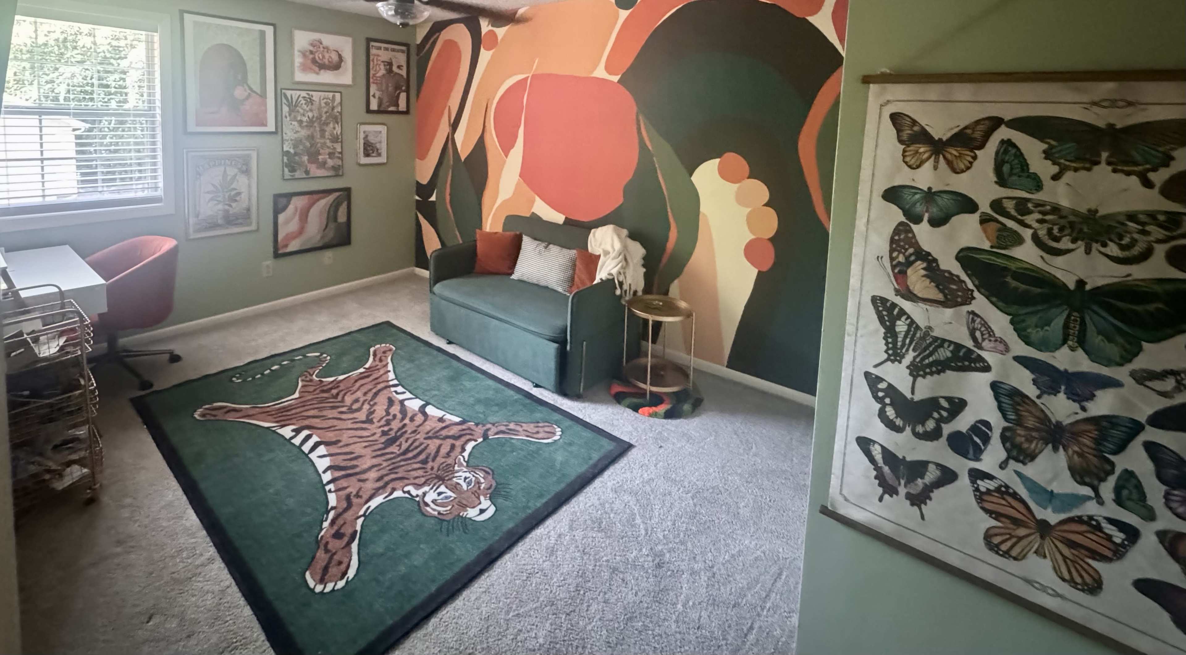 The image shows a bright room with a green accent wall featuring a large abstract mural, a green couch, a tiger-patterned rug, and framed artwork on the walls.