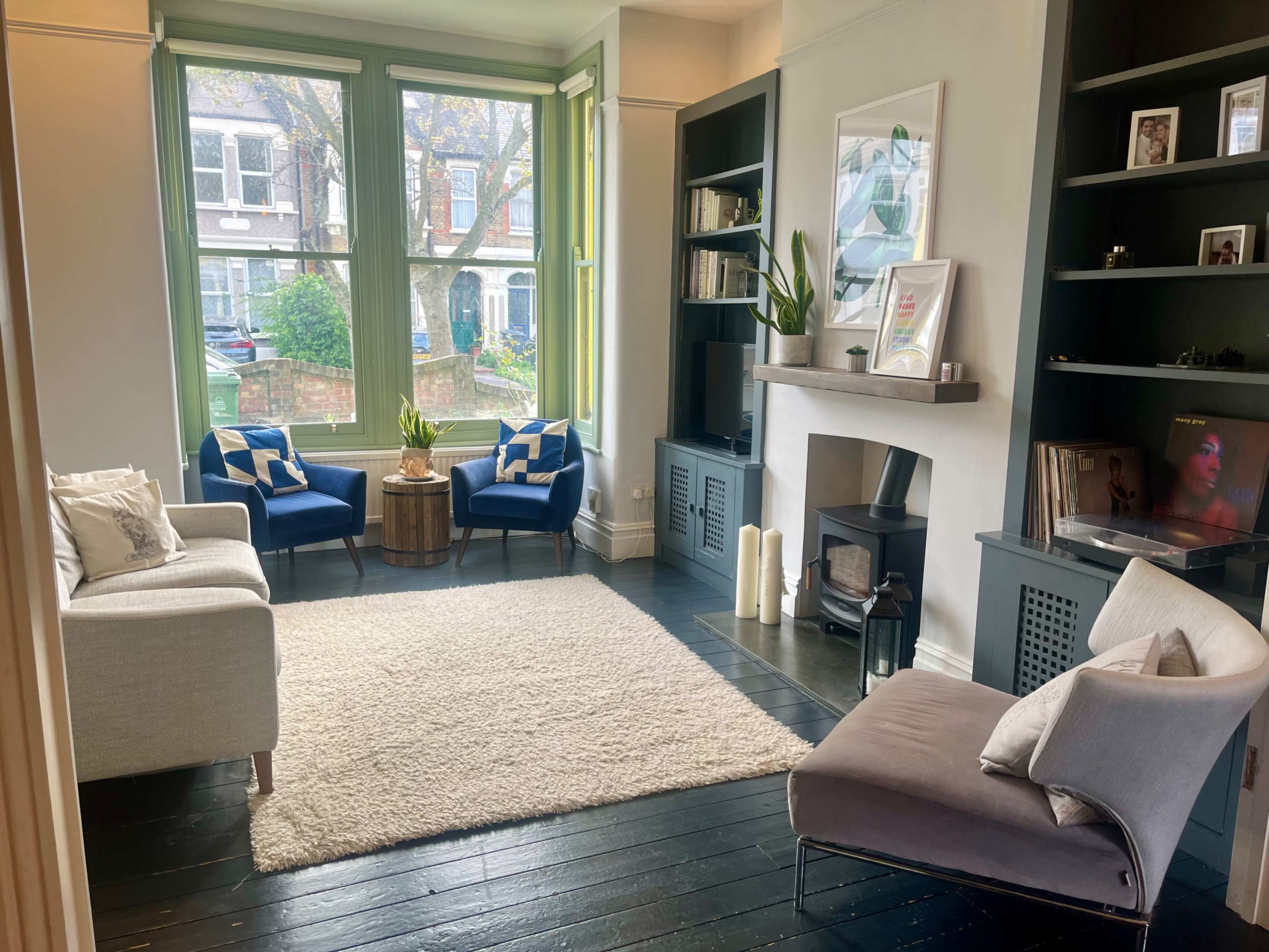 A cozy living room features two blue chairs, a coffee table, a black bookshelf, and a soft area rug.