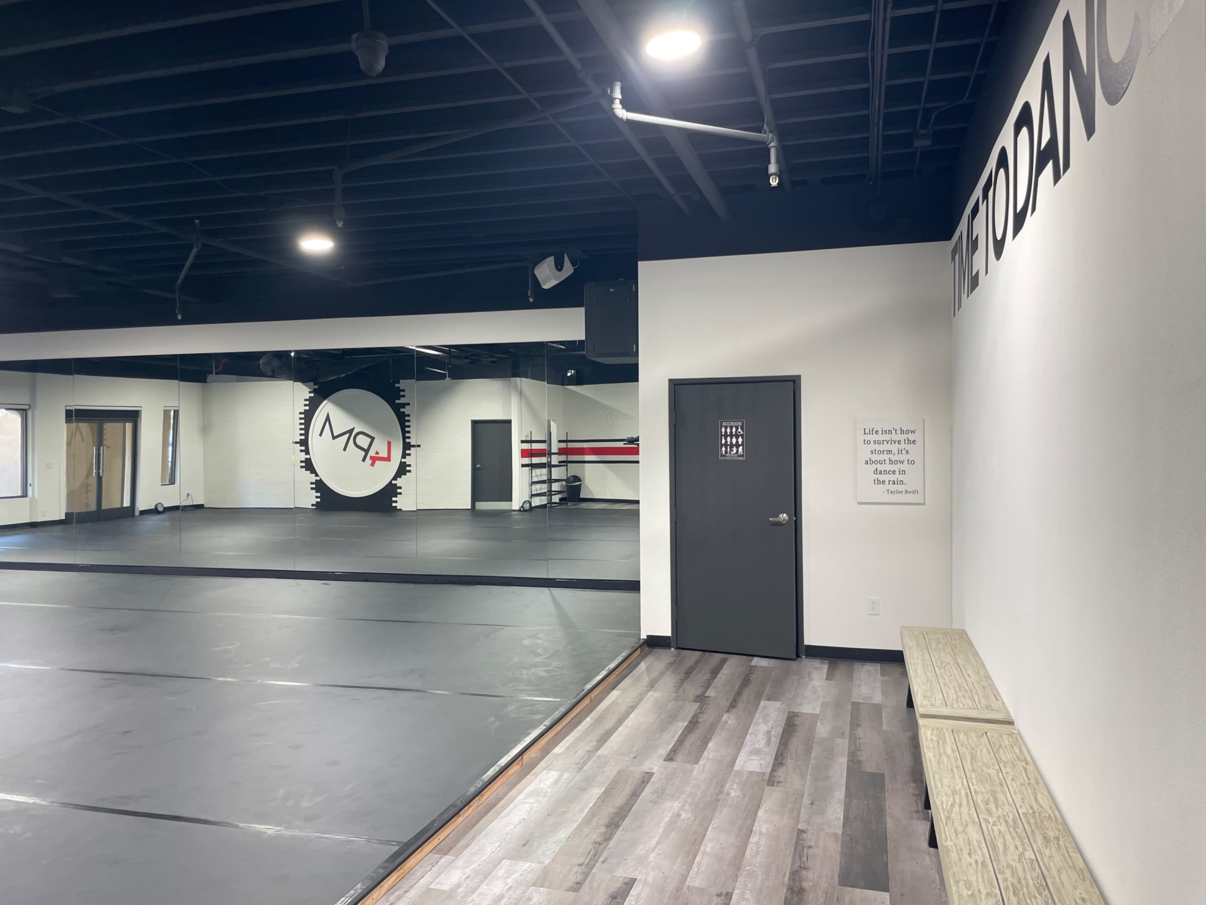 An empty dance studio with black flooring, mirrors, and a wall featuring the words "METODANCE."