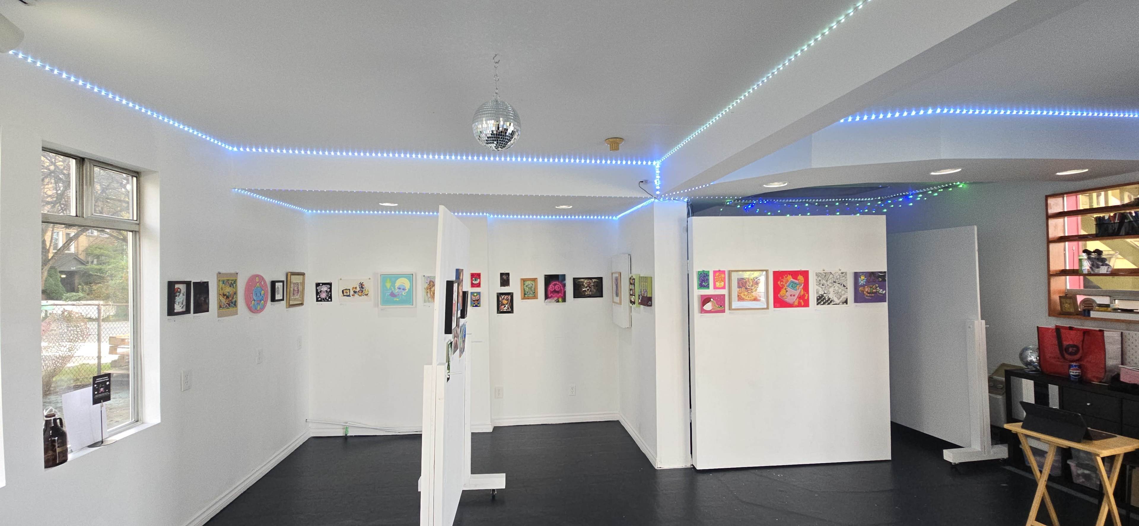 The image shows an art gallery with several colorful artworks displayed on white walls, illuminated by LED lights along the ceiling.