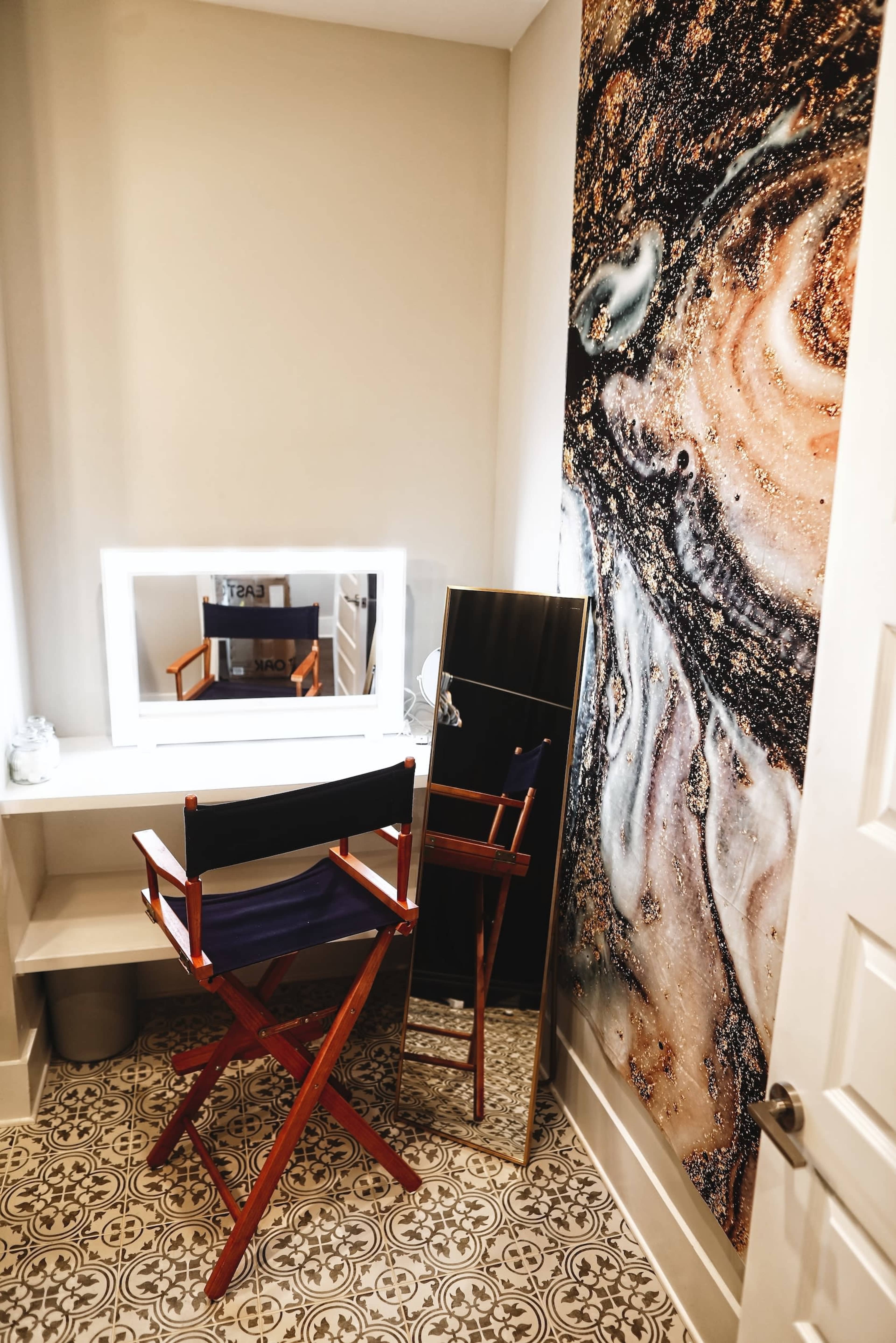A small vanity area features a makeup mirror, a wooden director's chair, and a decorative wall with a marbled design.