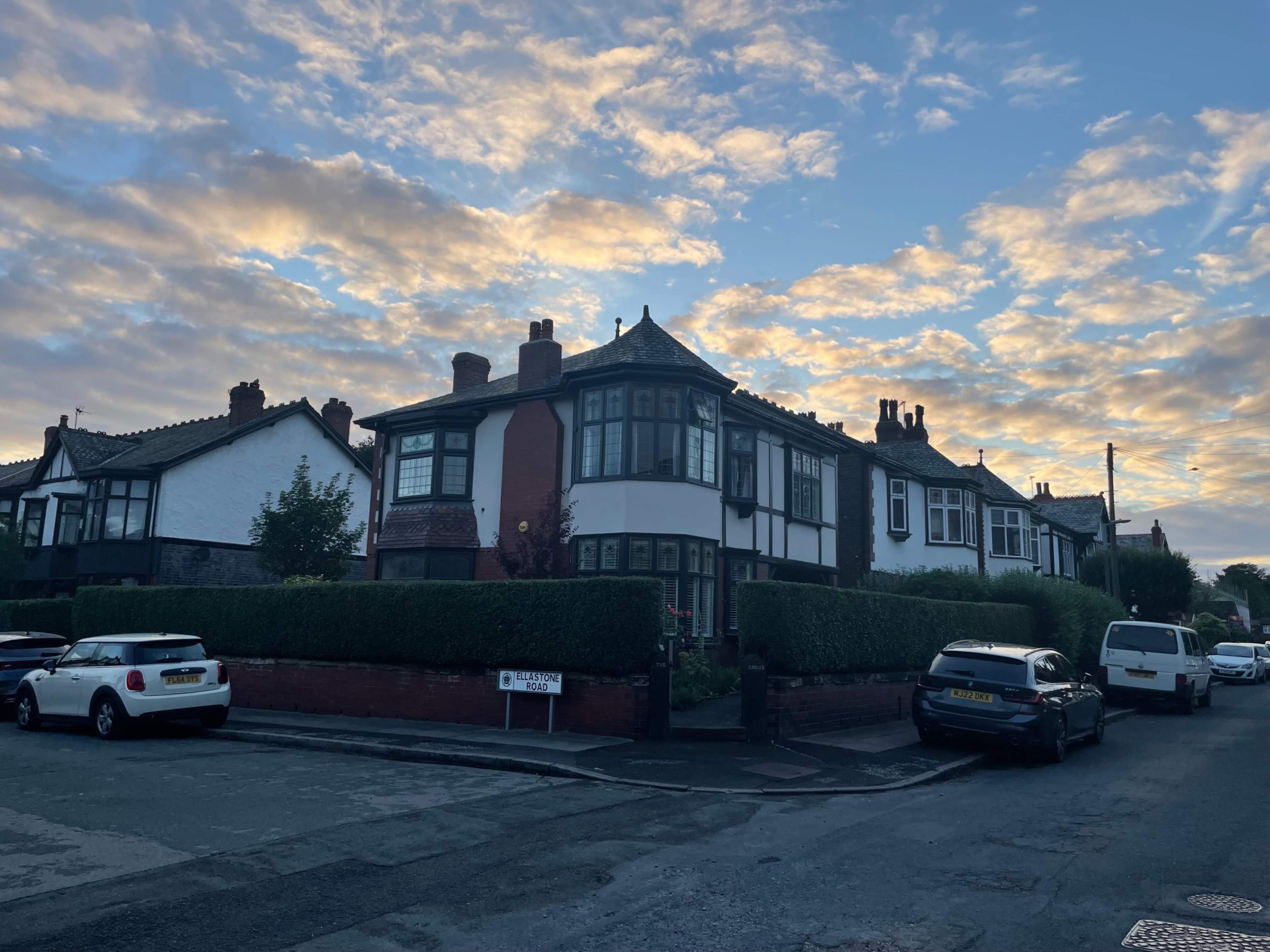 A row of houses with varied architectural styles lines a quiet street under a cloudy sky at dusk.