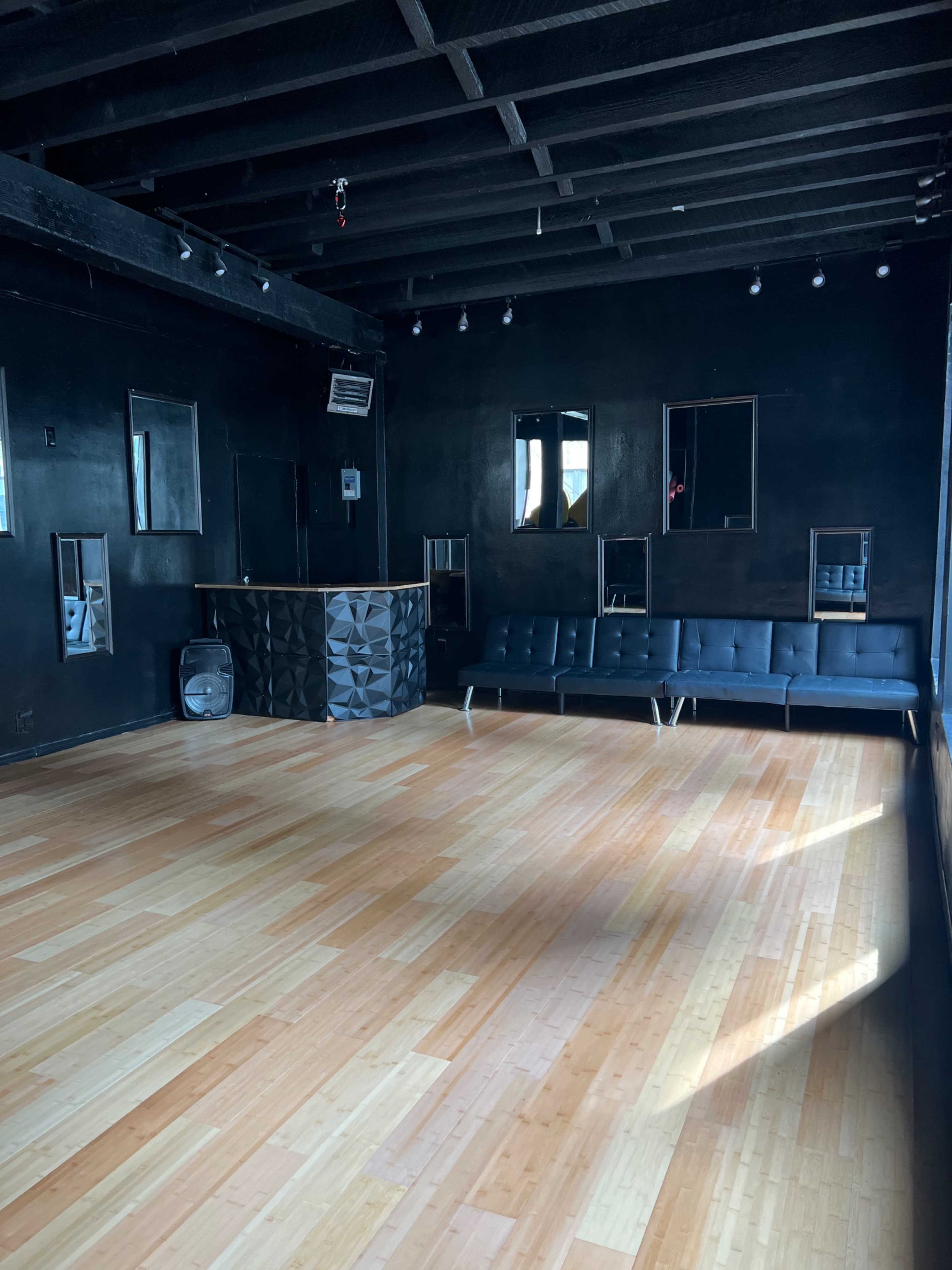 An empty room with a wooden floor, black walls, a bar counter, and a black sofa against one wall.